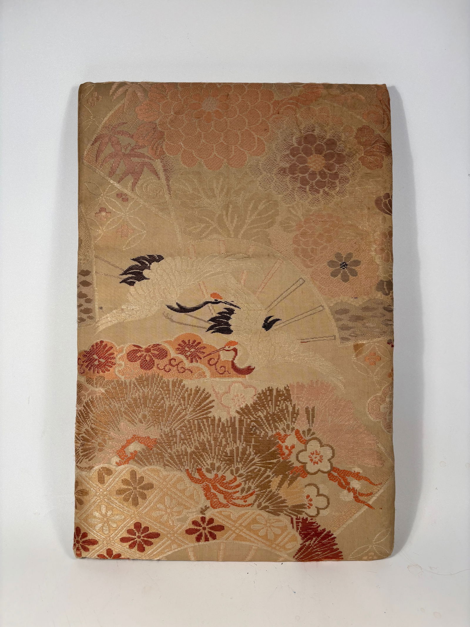 A Japanese Textile-Covered Album with Crane & Floral Motifs – Silk Brocade Cover: 19th Century; A vintage Japanese folding book or photo album, covered in elegant silk brocade fabric featuring a detailed and symbolic design of flying cranes among chrysanthemums, plum blossoms, and