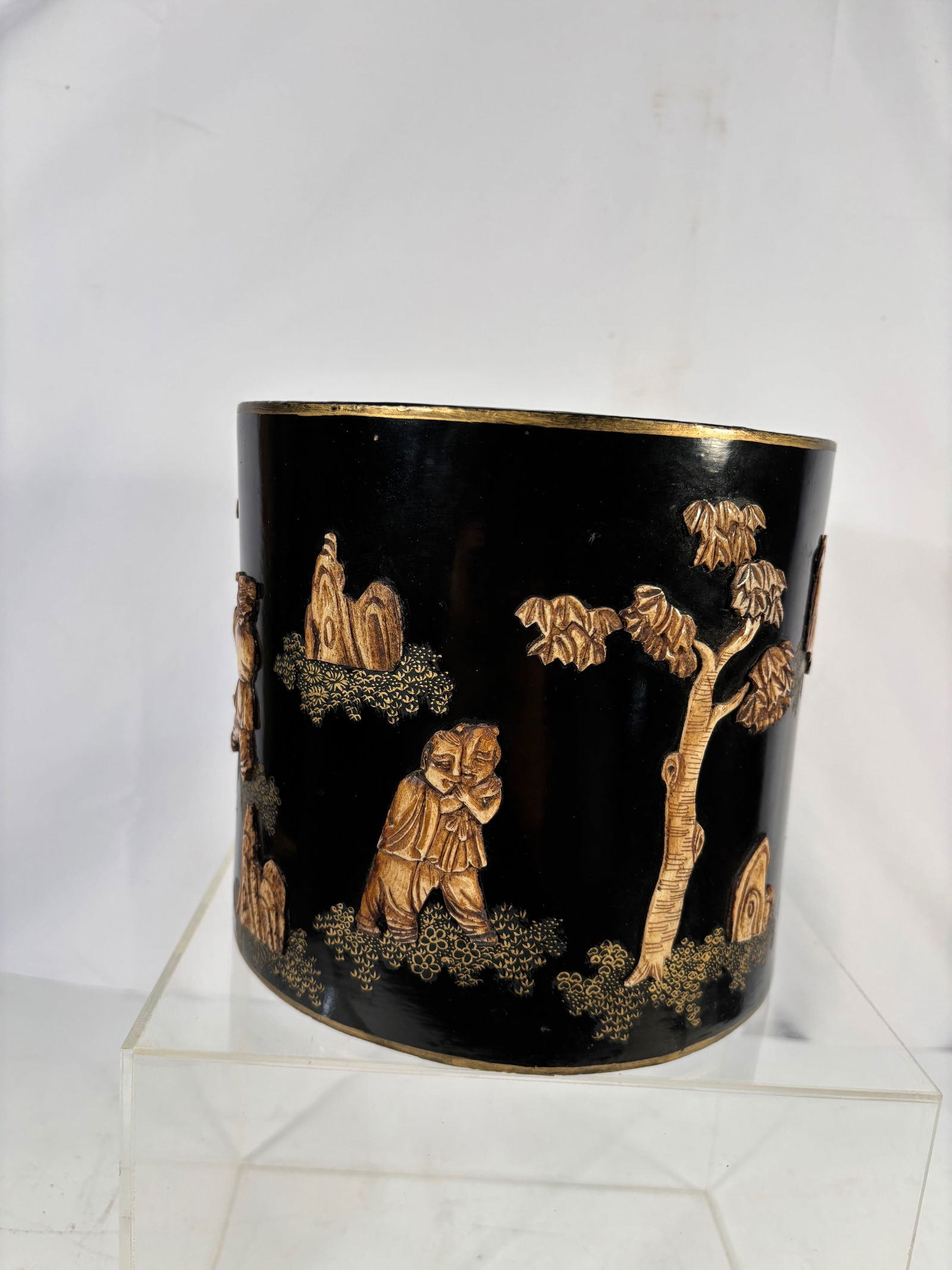 A Chinese Black Lacquer Brush Pot with Gilt Figural Decoration: 20th century, Chinese black lacquer brush pot decorated in relief with gilt figures in a landscape. Likely resin or composite material with lacquer coating.The underside bears a “Made in China&rdquo