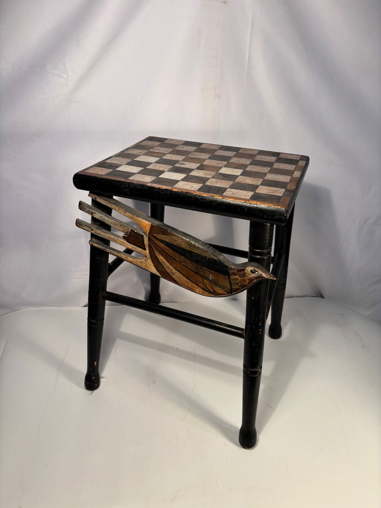 Folk Art Game Table with Checkerboard Top and Carved Bird Motif: Decorative folk art table featuring a checkerboard game top above a painted and carved bird motif mounted to the apron. The bird is rendered in layered wood with carved detailing to the body, wing,