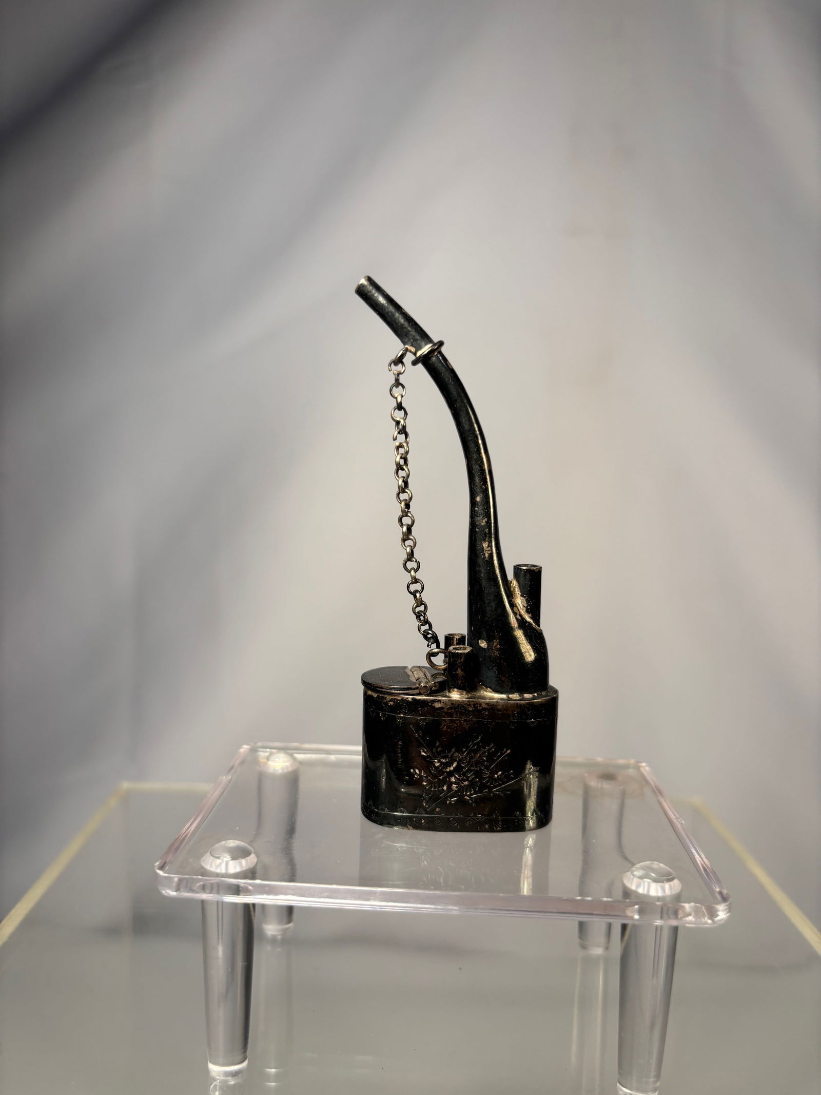 A Chinese Silver Metal Opium Pipe Bowl with Hinged Cover: Qing dynasty(1644-1912); Chinese silver opium pipe bowl, late Qing dynasty. The bowl features engraved decoration and a hinged cover with an attached safety chain. Height: 3.75 inches.