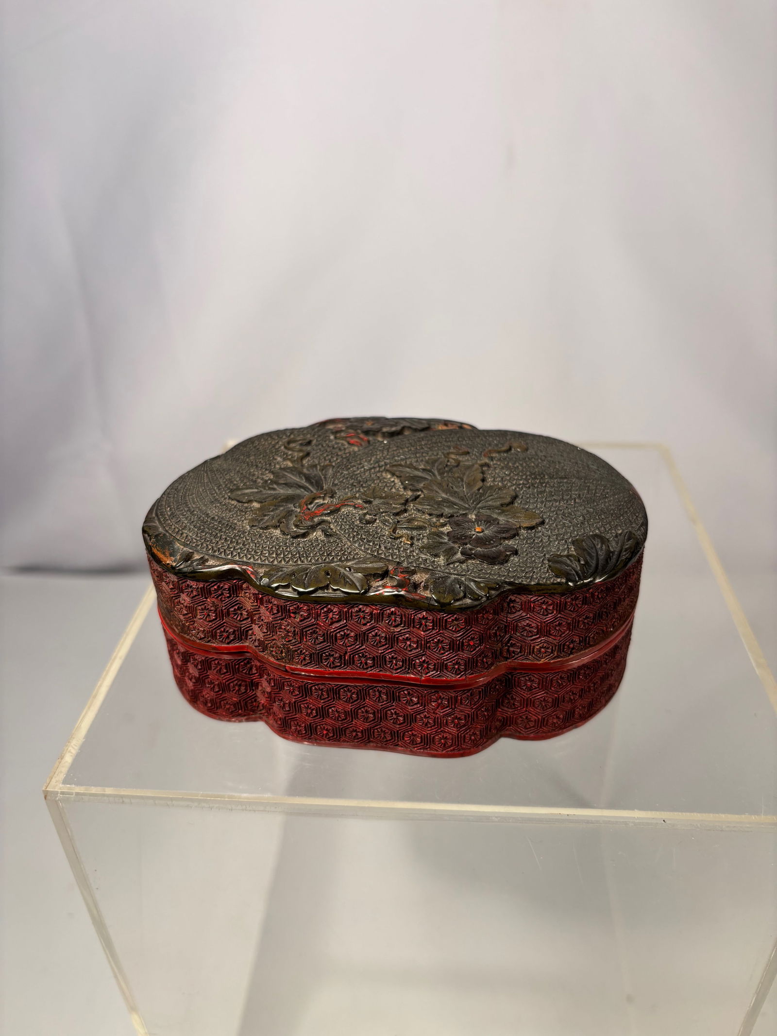 A Chinese Ticai Lacquered Box with Floral and Vine Motifs: A Chinese carved lacquer box of lobed form, finished in contrasting black and red lacquer. The exterior is decorated with finely carved floral and vine motifs set against a dense, textured ground, whi