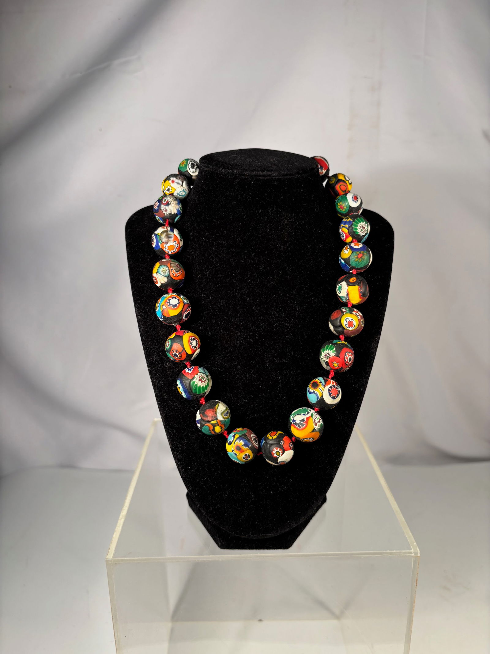 A Vintage Millefiori Murano-Style Glass Bead Necklace: Strand of large millefiori glass beads decorated with colorful floral and geometric cane patterns on a dark glass ground. Likely Venetian or Murano-style production.Each bead displays unique multicolo
