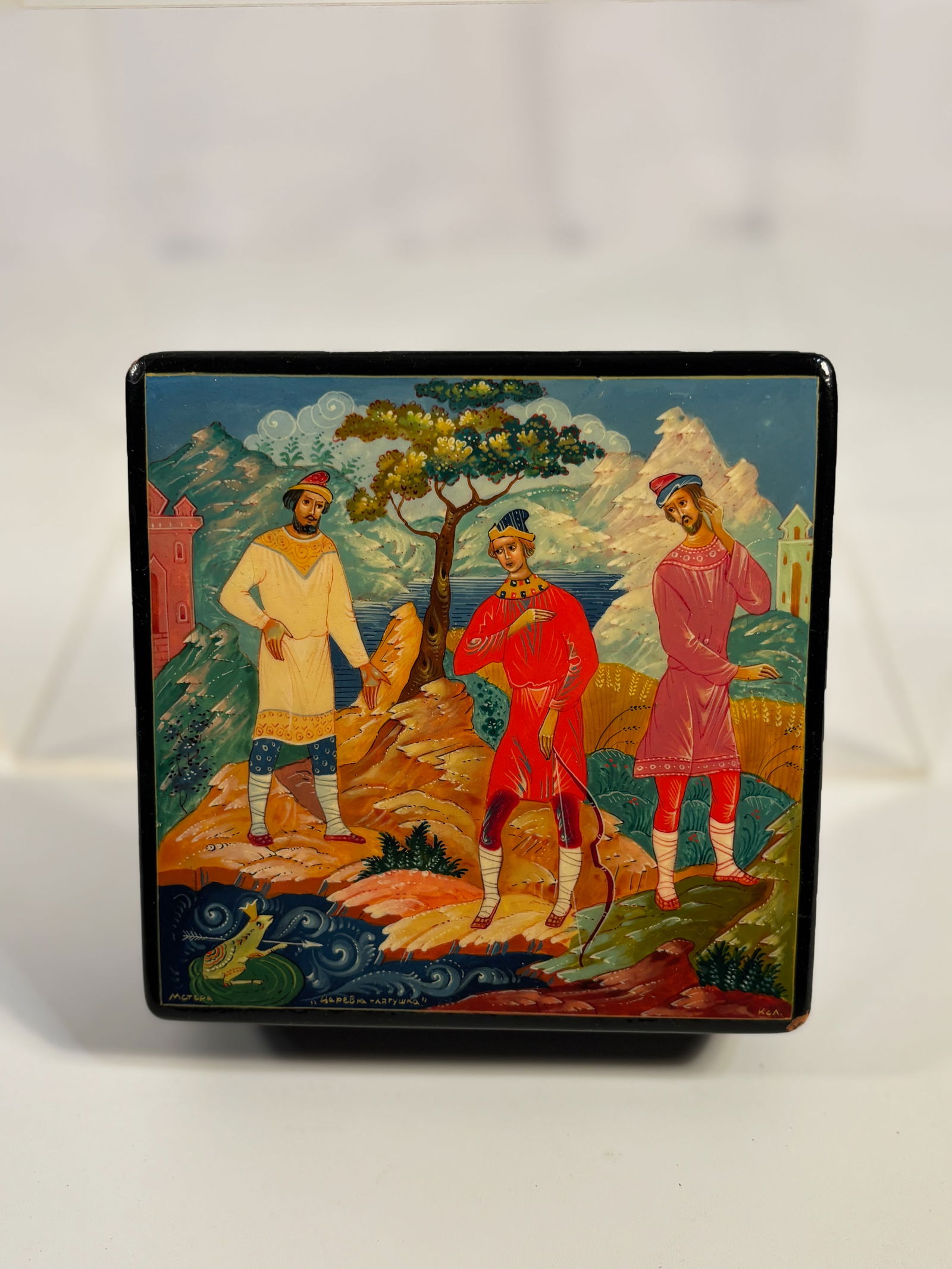 Russian Lacquer Miniature Box, Palekh School, Folk Tale Scene, 20th Century: A Russian hand-painted lacquer miniature box, of rectangular form, the hinged lid depicting a vivid folk tale scene with three figures before a stylized tree and castle, one figure holding a bow. Pain