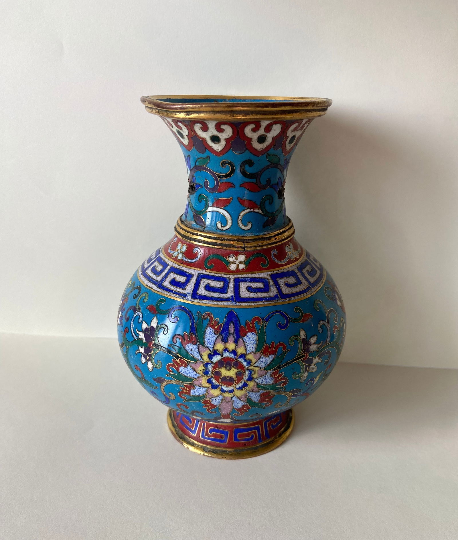 A Chinese cloisonné enamel vase: 18th Century; Of baluster form with flaring neck, decorated with multicolored lotus scrolls on a turquoise ground, bordered with ruyi and key-fret bands. Gilt metal mounts and base. Dimensions?Height:
