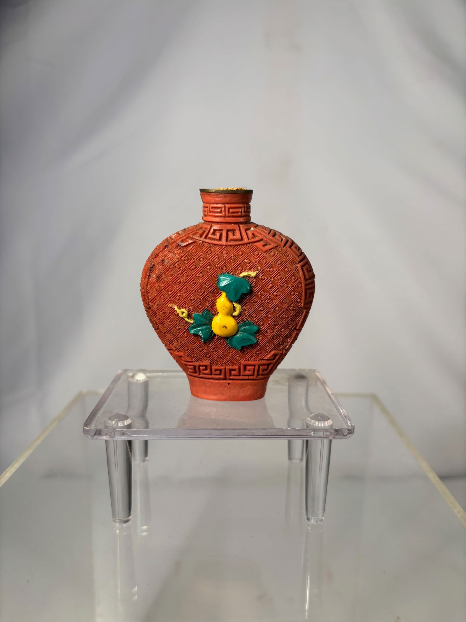 A Chinese Cinnabar-Style Snuff Bottle with Double Gourd Motif, 20th Century: Molded cinnabar-style snuff bottle of flattened ovoid form, decorated overall with a repeating leiwen (thunder) pattern and applied with a raised double gourd and leafy vine motif in contrasting