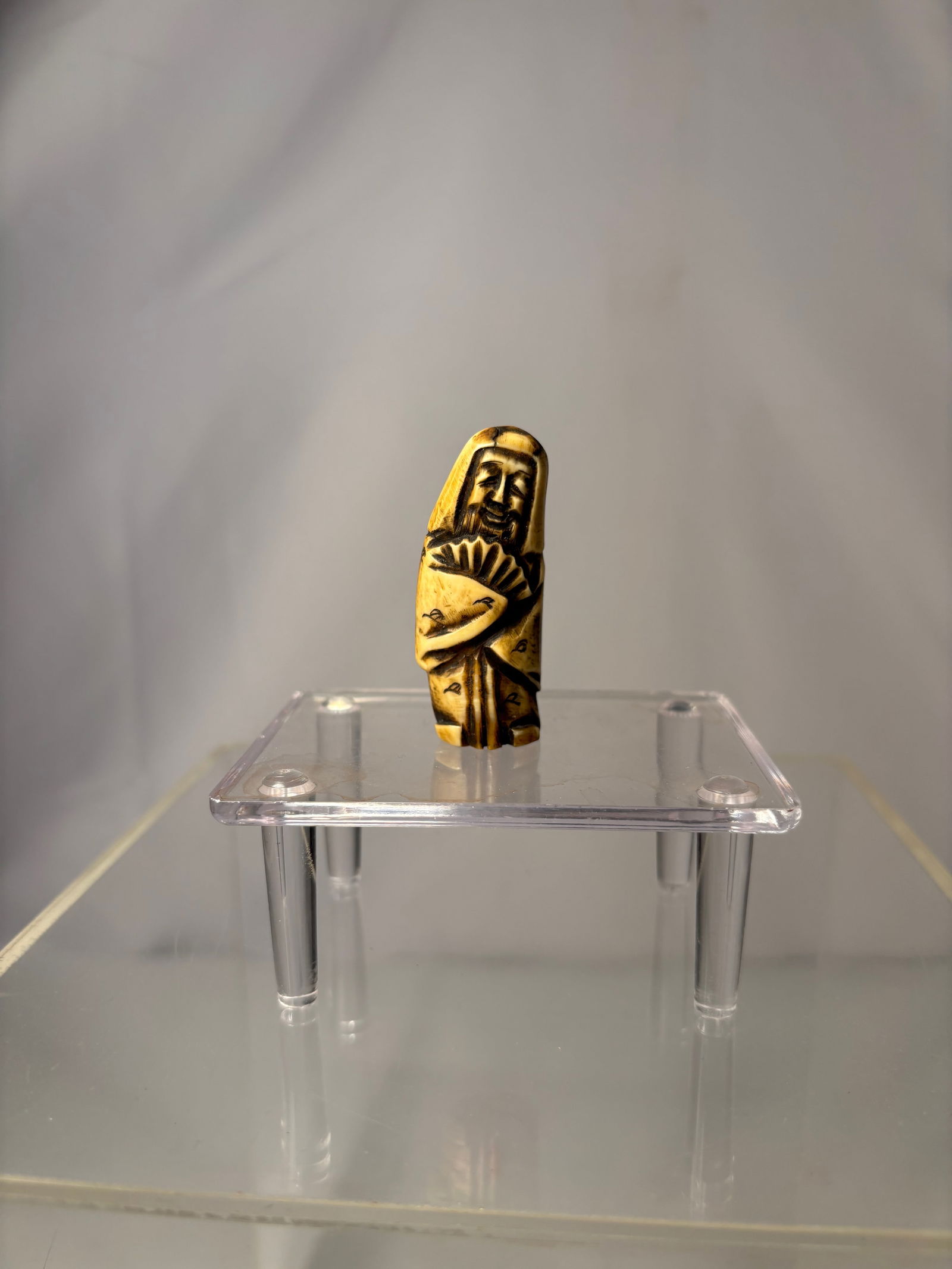 A Japanese Figural Netsuke, Carved Bone Standing Figure, Signed (Hisakazu / Ky?ichi): 19th century, A Japanese figural netsuke carved from bone, depicting a standing human figure with a humorous expression and stylized features. The carving includes two himotoshi to the reverse, confir