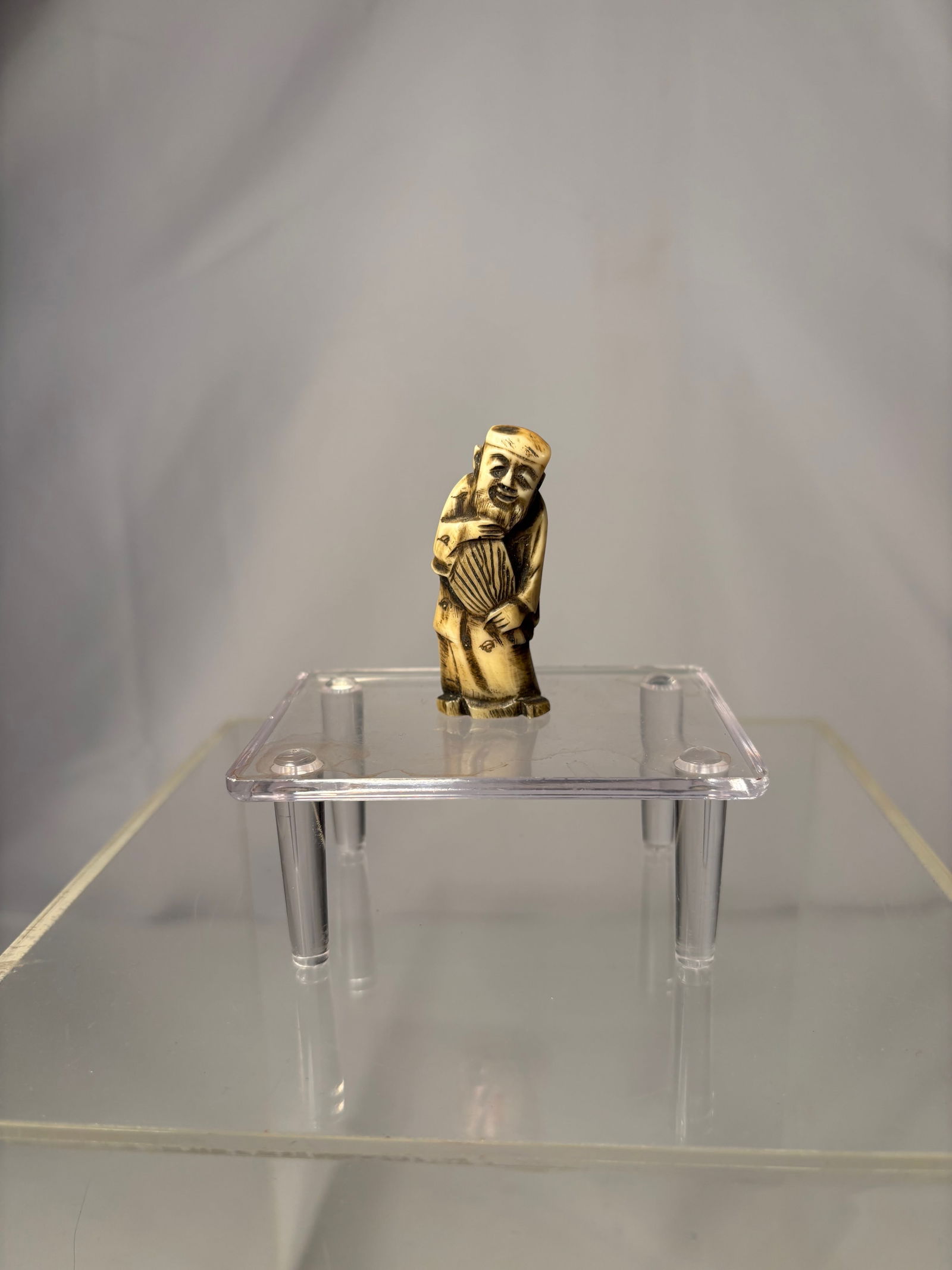 A Japanese Figural Netsuke, Carved Bone Standing Figure, Signed (Hisakazu / Ky?ichi): 19th century, A Japanese figural netsuke carved from bone, depicting a standing human figure with a humorous expression and stylized features. The carving includes two himotoshi to the reverse, confir