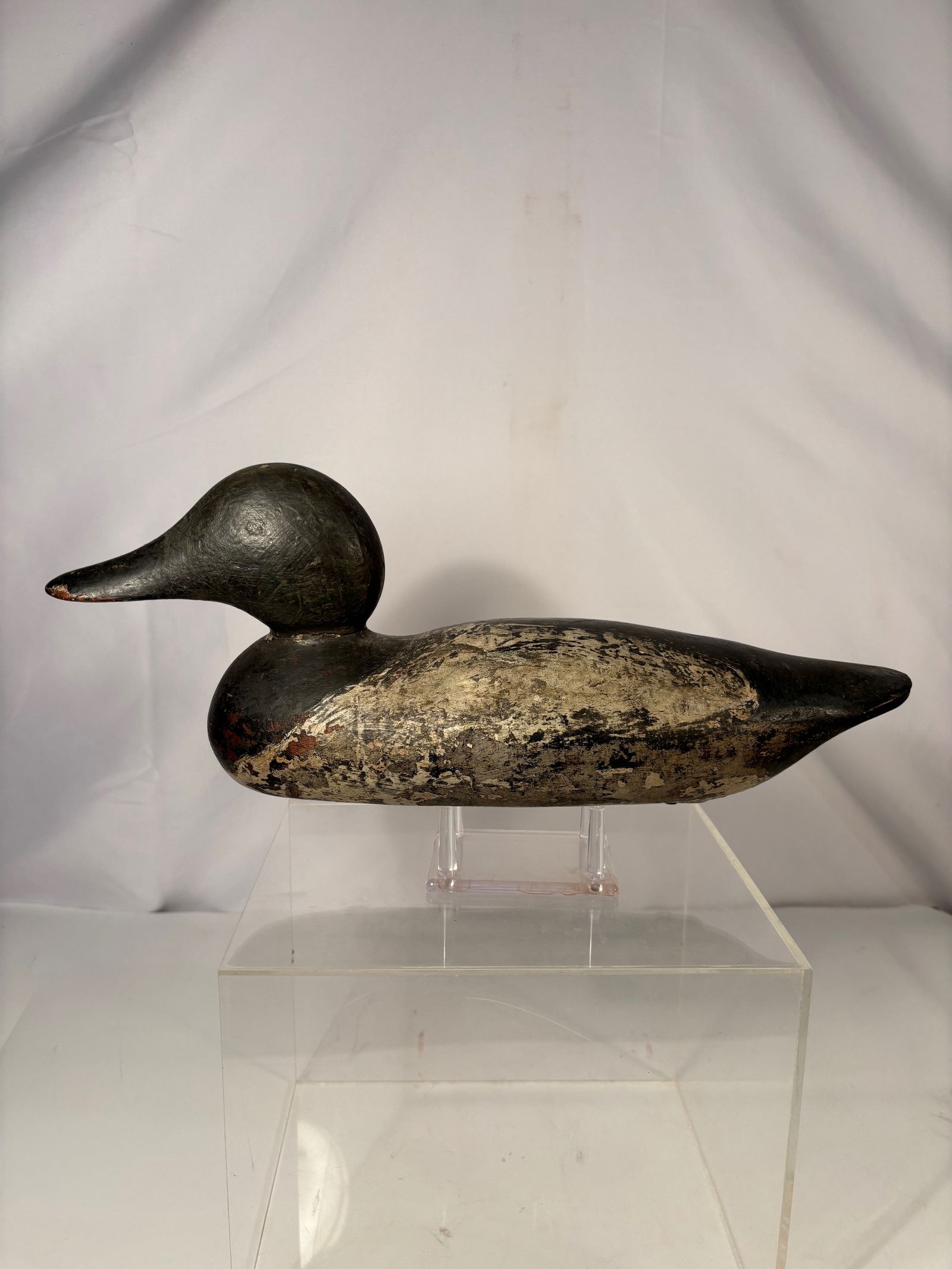 A Hand-Carved Duck Decoy with Weighted Keel, Branded “AN,?? Early 20th Century: Hand-carved wooden duck decoy with rounded head and streamlined body, retaining a heavily weathered painted surface. The underside bears a branded mark reading “AN” and is fitted with a weight