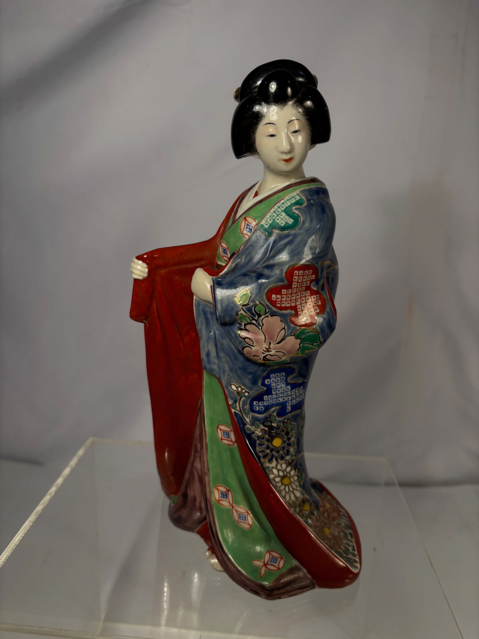 A Japanese Kutani Style Porcelain Figure of Geisha: A finely modeled Japanese porcelain figure depicting a standing geisha in traditional kimono. The robe richly decorated in Kutani style enamels with floral motifs, geometric reserves, and gilt accents