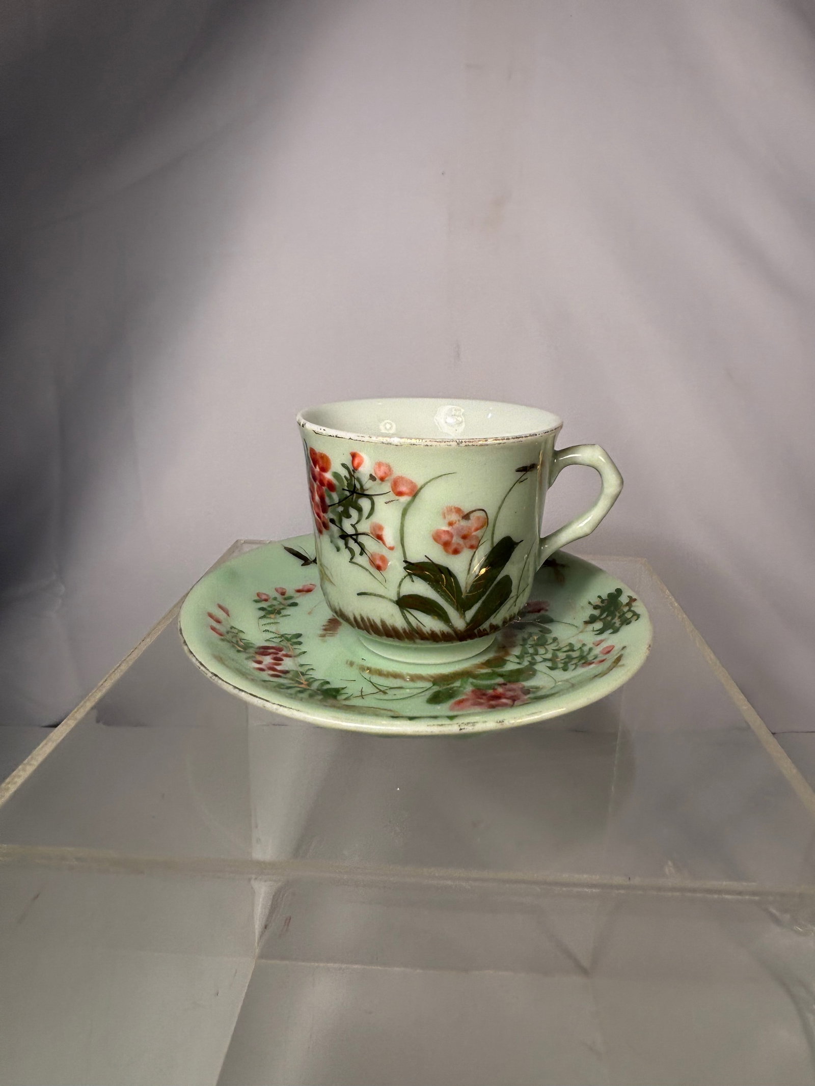 A Japanese Porcelain Cup and Saucer with Floral and Insect Decoration, Meiji Period (1868–1912): A Japanese porcelain cup and saucer, decorated in overglaze enamels on a pale celadon-green ground. The exterior of the cup and the surface of the saucer are finely painted with flowering plants, foli