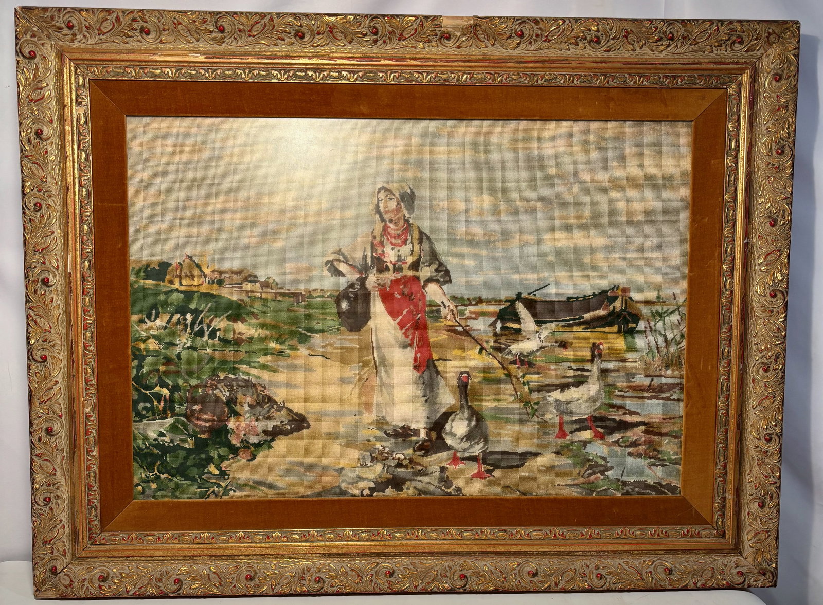 A European Pictorial Tapestry / Needlework Wall Hanging with Rural Figure, 19th Century: Continental European pictorial tapestry or needlework wall hanging, 19th century, depicting a rural genre scene of a woman feeding geese along a shoreline with boats and landscape beyond. Woven in mut