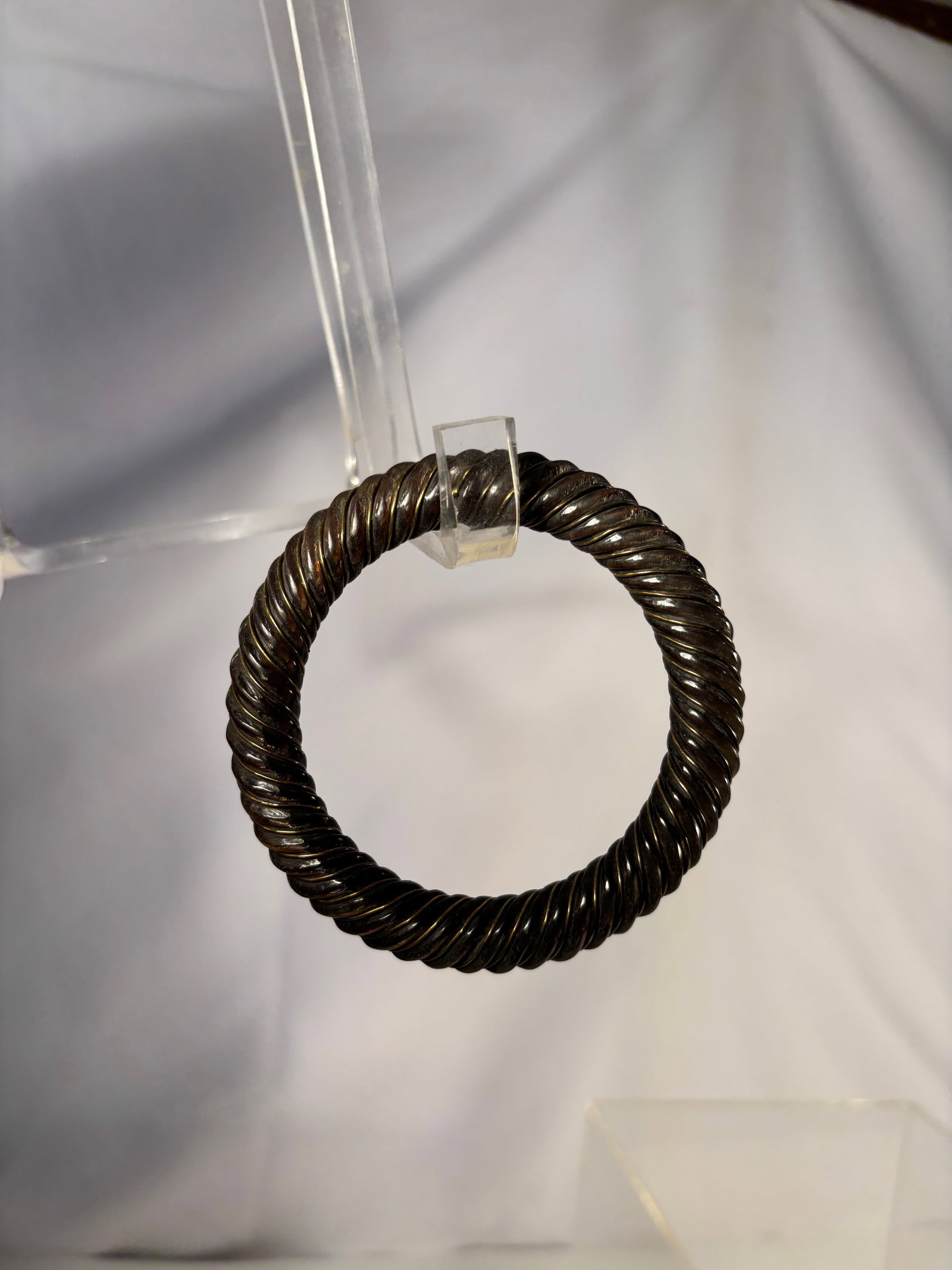 A Chinese Carved Ox Horn Bracelet Inlaid with Brass Wire: A Chinese ox horn bracelet finely formed into a circular bangle and decorated with tightly wrapped inlaid copper wire in a continuous twisted rope pattern. The dark horn ground provides strong