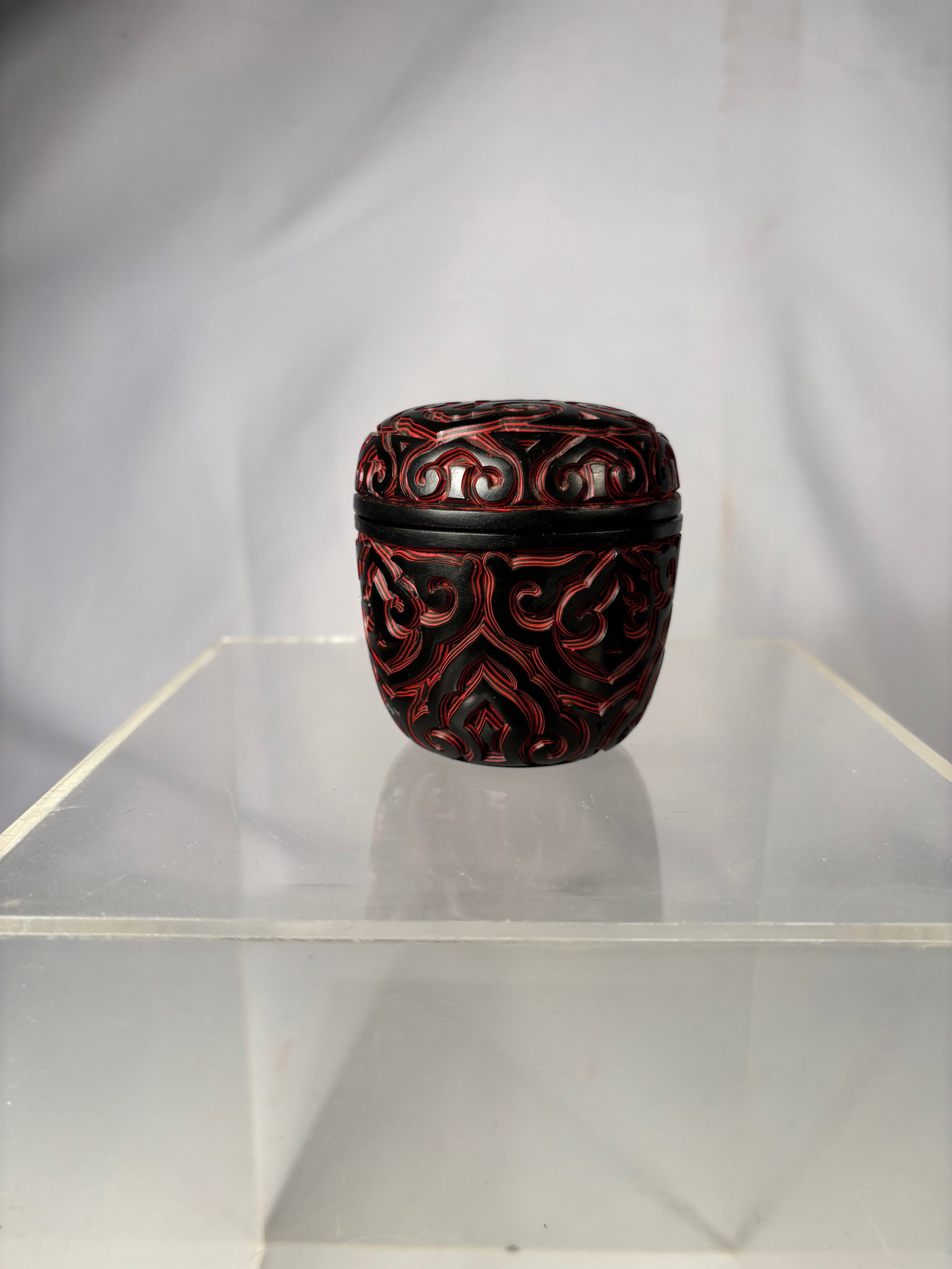 A Chinese Black and Red Carved Lacquer Circular Covered Box: Chinese black and red carved lacquer circular covered box. The domed cover is decorated with an intricate scrolling pattern carved in red lacquer against a black ground, centered with a star-shaped mo