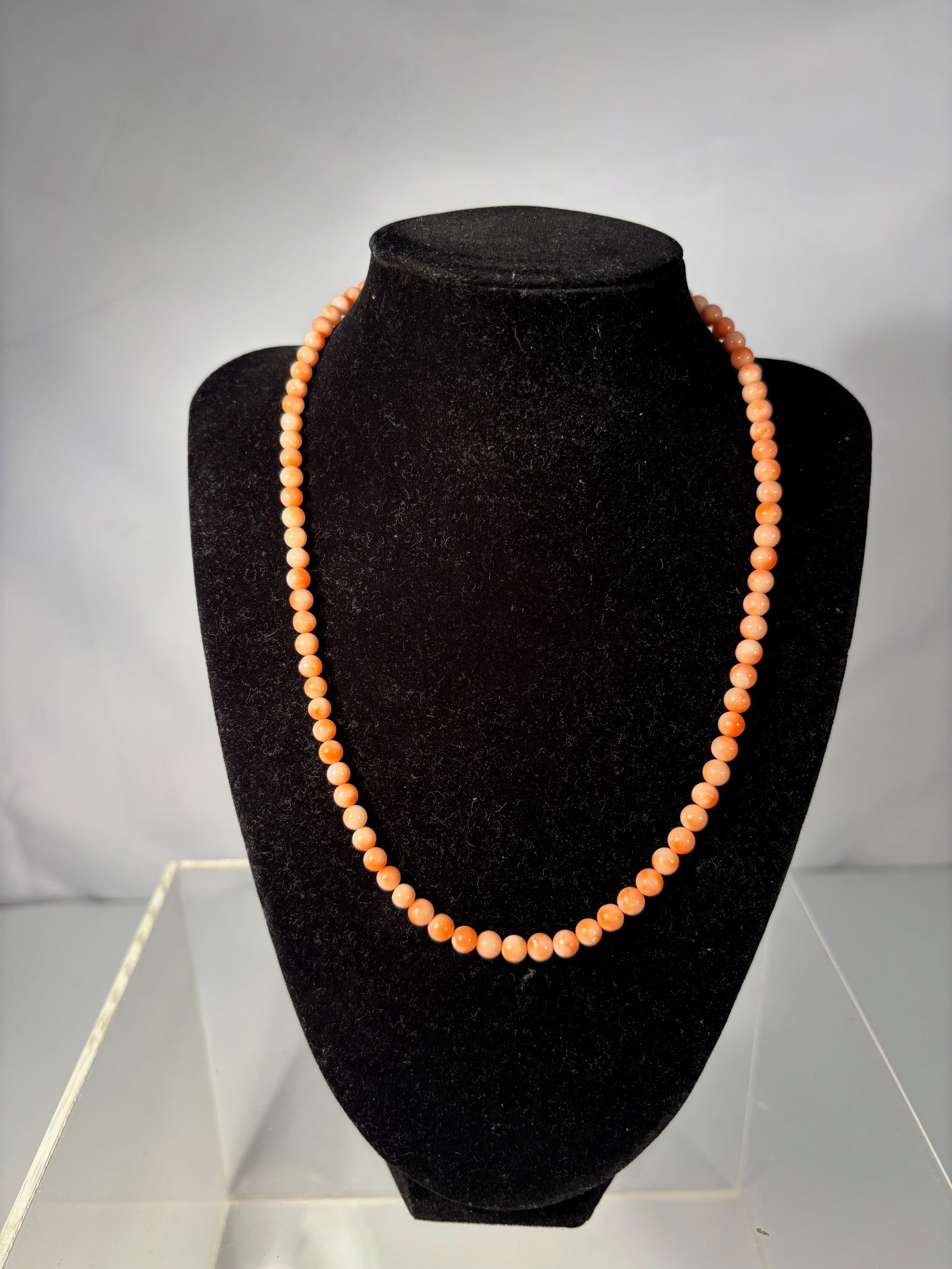 A Salmon Coral Bead Necklace: Composed of a single strand of well-matched round coral beads of uniform salmon-pink to light orange hue, smoothly polished and strung with a gilt metal clasp enhanced with gold-tone and faceted cryst