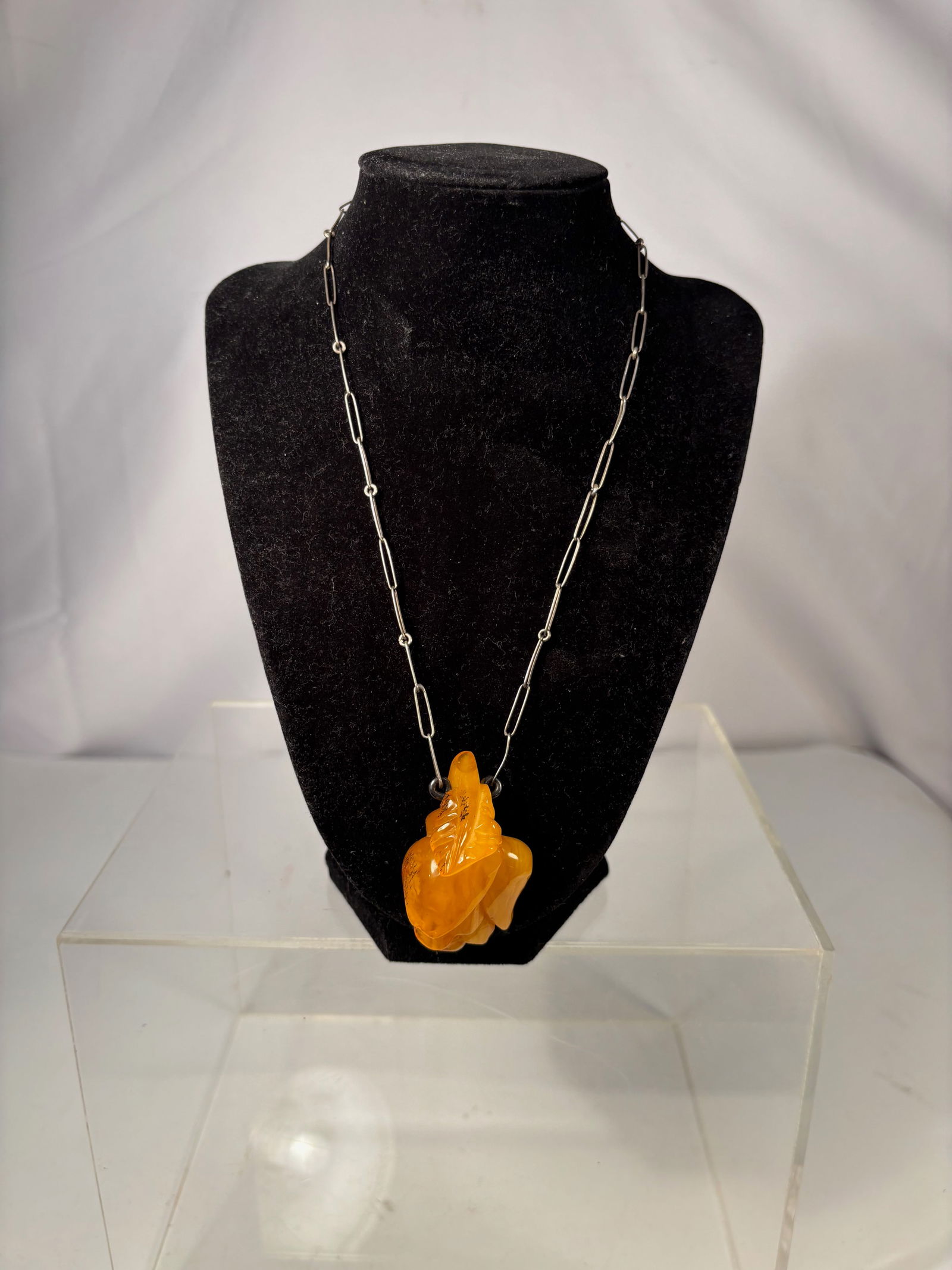 A Butterscotch Amber Carved Pendant on Silver-Tone Chain: This necklace features a carved butterscotch amber pendant, displaying a rich opaque yellow to warm honey tone characteristic of classic butterscotch amber. The pendant is carved in an organic,