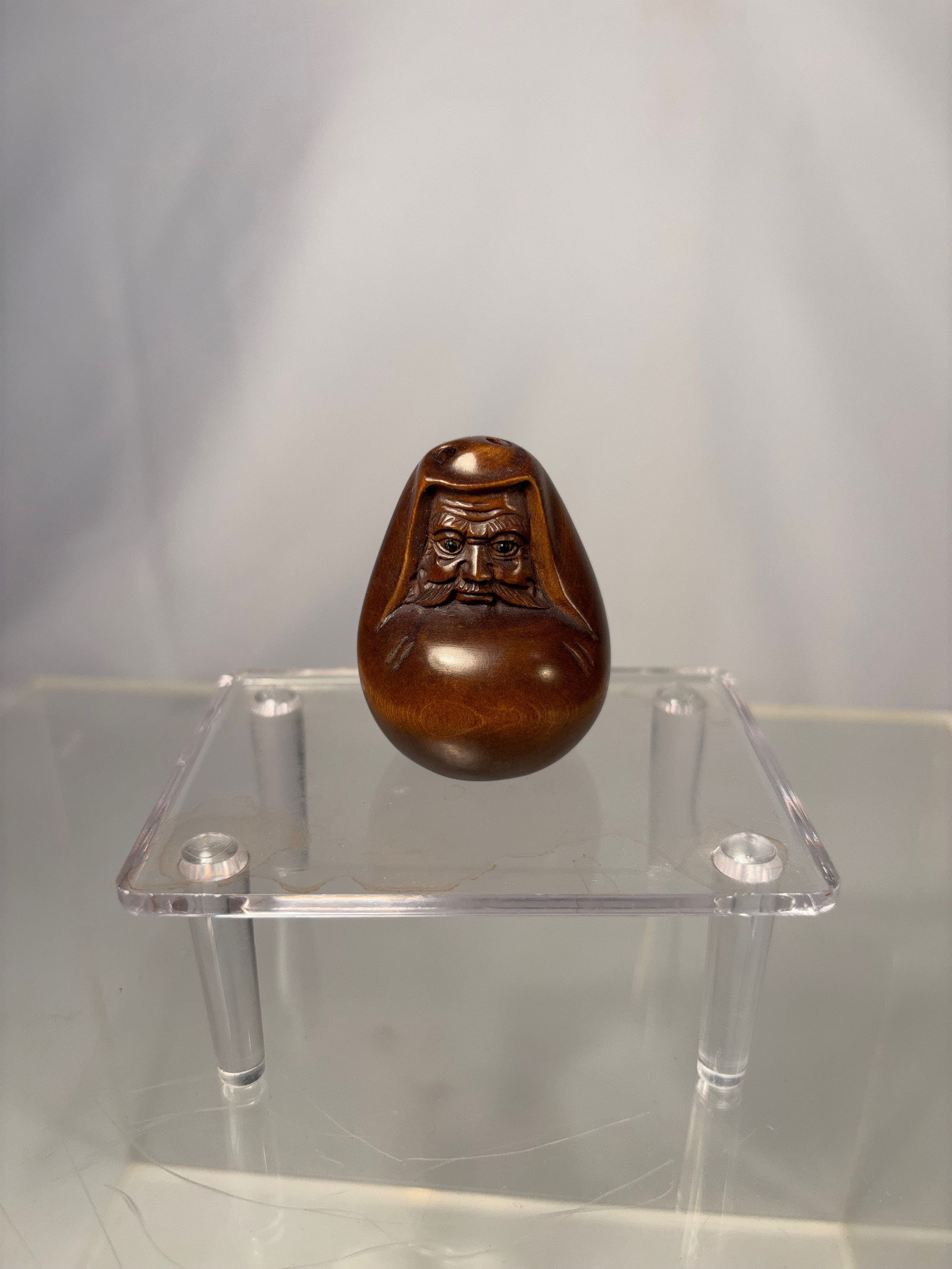 A Japanese Carved boxwood Netsuke, Signed Gyokumatsu meiji period or later: 19th -20th century, Carved wooden netsuke depicting a smiling male face, modeled with rounded features and a polished surface. The underside bears an incised signature reading Gyokumatsu (???). The wo