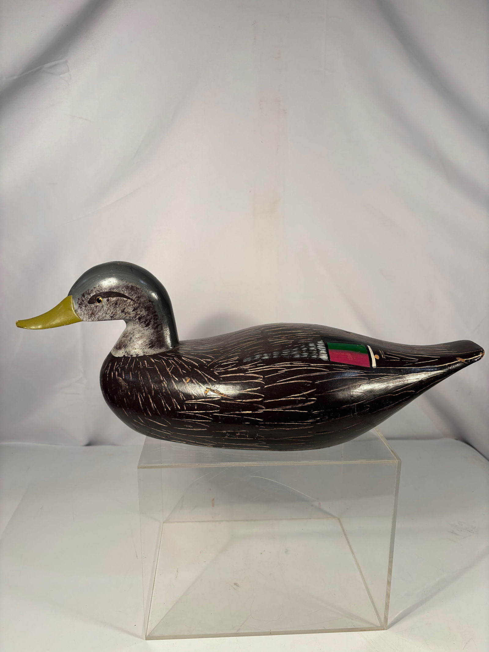A Hand-Carved Duck Decoy with Incised Feather Detail, Mid-20th Century: Hand-carved wooden duck decoy with stylized form and finely incised feather detailing, featuring a painted surface with decorative coloration to the body. American folk art example, likely mid-20th