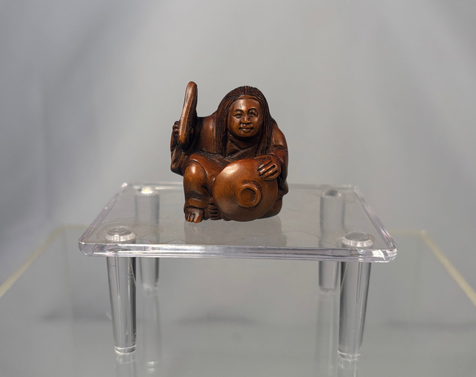 A Japanese Boxwood Netsuke, Figure with Jar, Signed Ishikawa,: Meiji period (19th century), A finely carved Japanese boxwood netsuke depicting a seated figure holding a jar, rendered with a warm patina and expressive facial features. The carving shows careful att