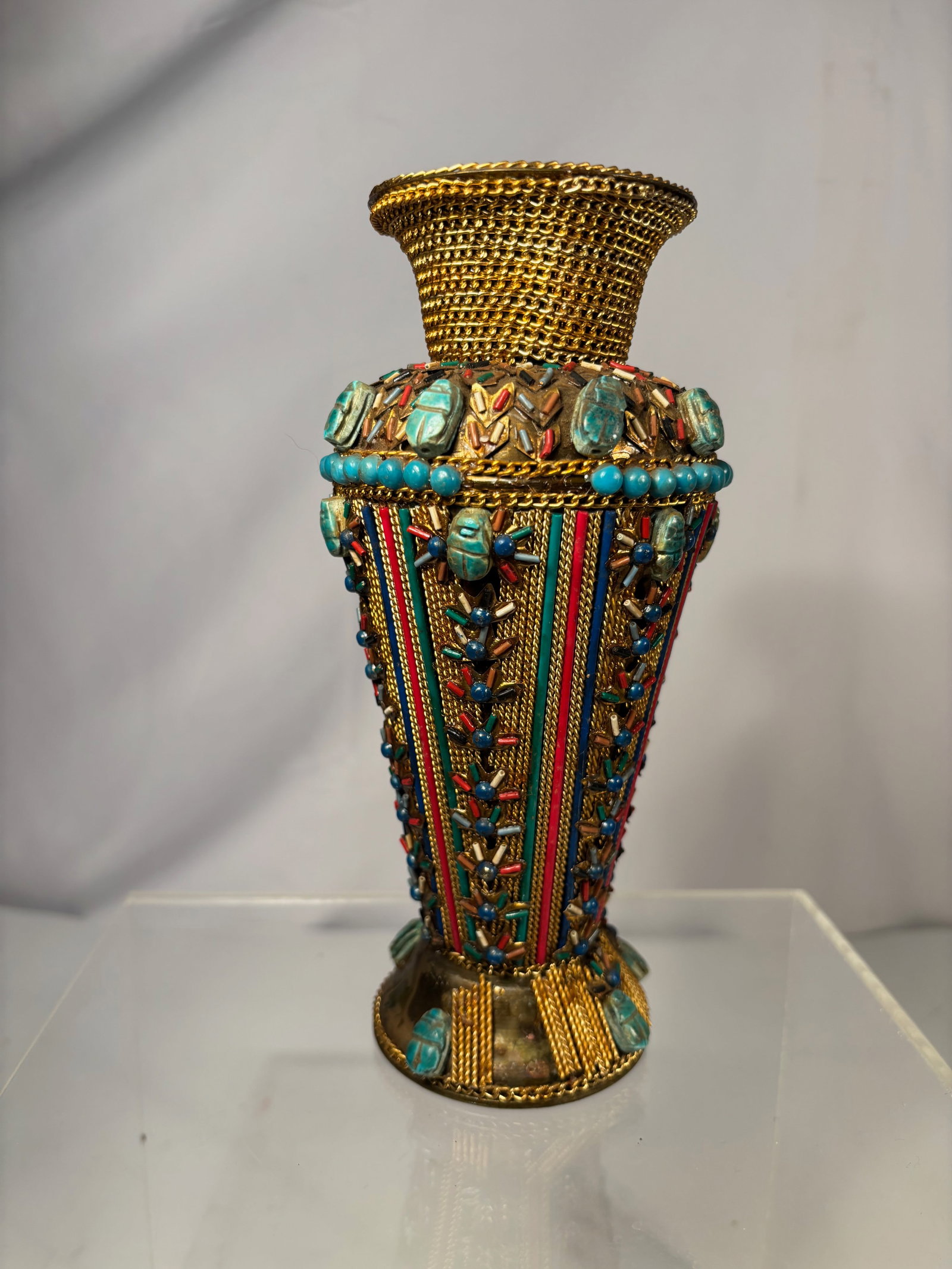 An Egyptian Revival Jeweled Brass Vase with Scarab Motifs, 20th Century: Egyptian Revival jeweled brass vase of flared form, richly decorated with applied scarab motifs, turquoise-colored cabochons and beadwork, and polychrome enamel accents. The exterior features vertical