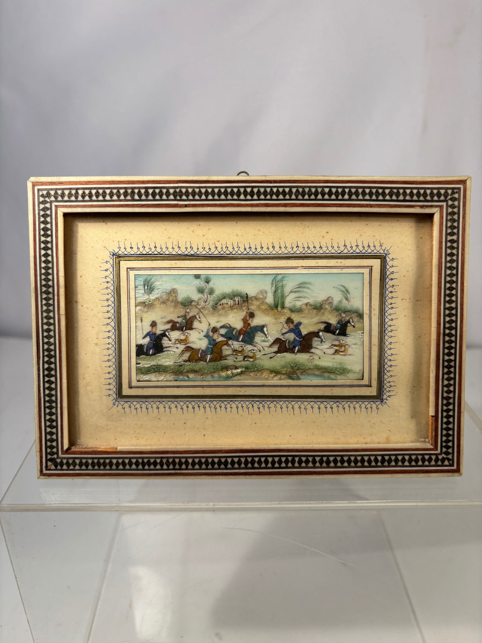 Persian Miniature Painting of Horsemen Hunting Scene, Framed: A finely executed Persian miniature painting depicting a dynamic hunting scene with mounted horsemen pursuing game across a stylized landscape. The composition is rich in movement and detail, showing