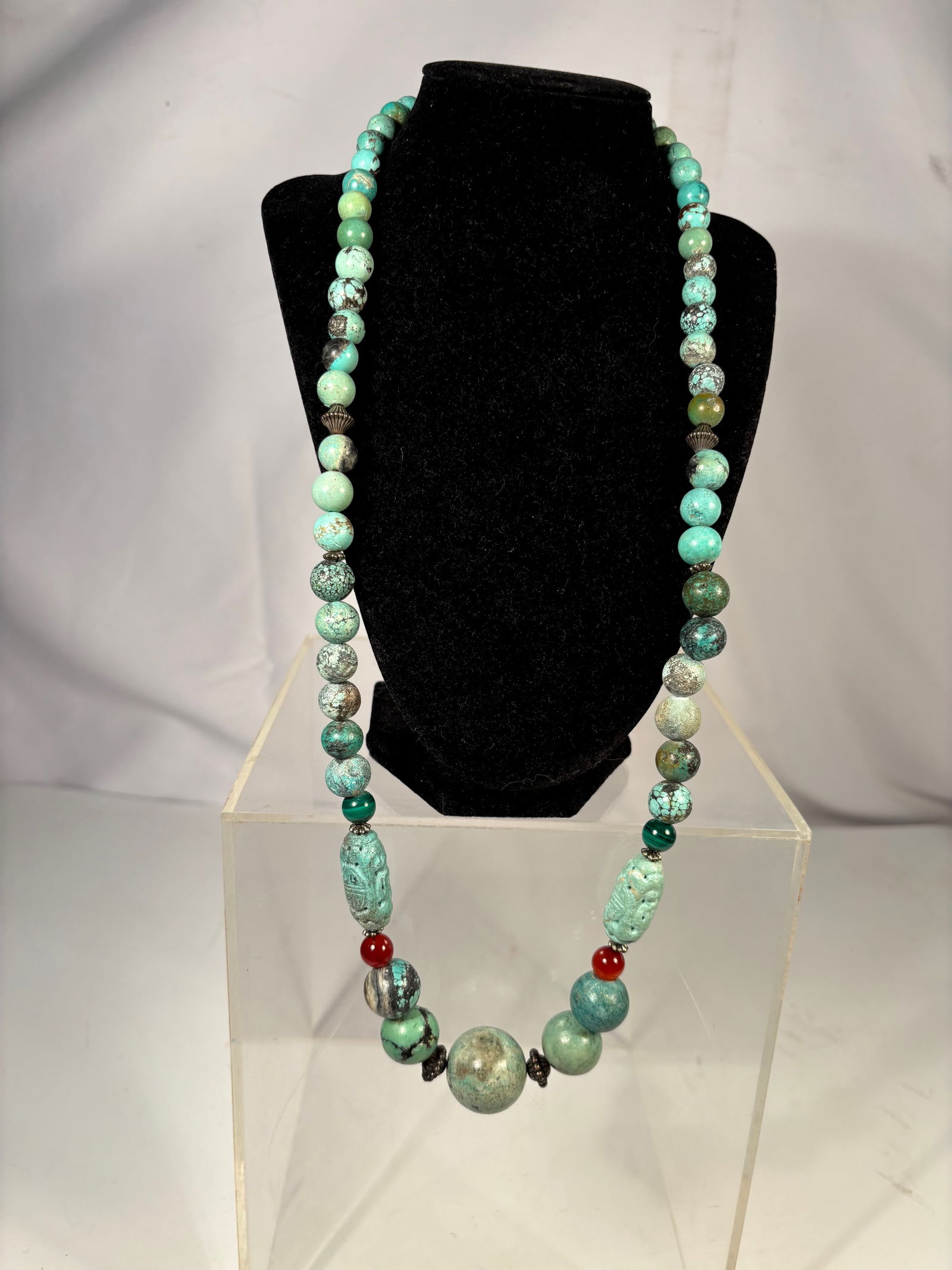 A Long Tibetan Turquoise and Carnelian Necklace with Two Antique Carved Turquoise Beads: Necklace composed of turquoise beads with natural matrix, two antique carved turquoise barrel beads, carnelian accent beads, malachite bead, and silver spacers. Total necklace length approximately 30