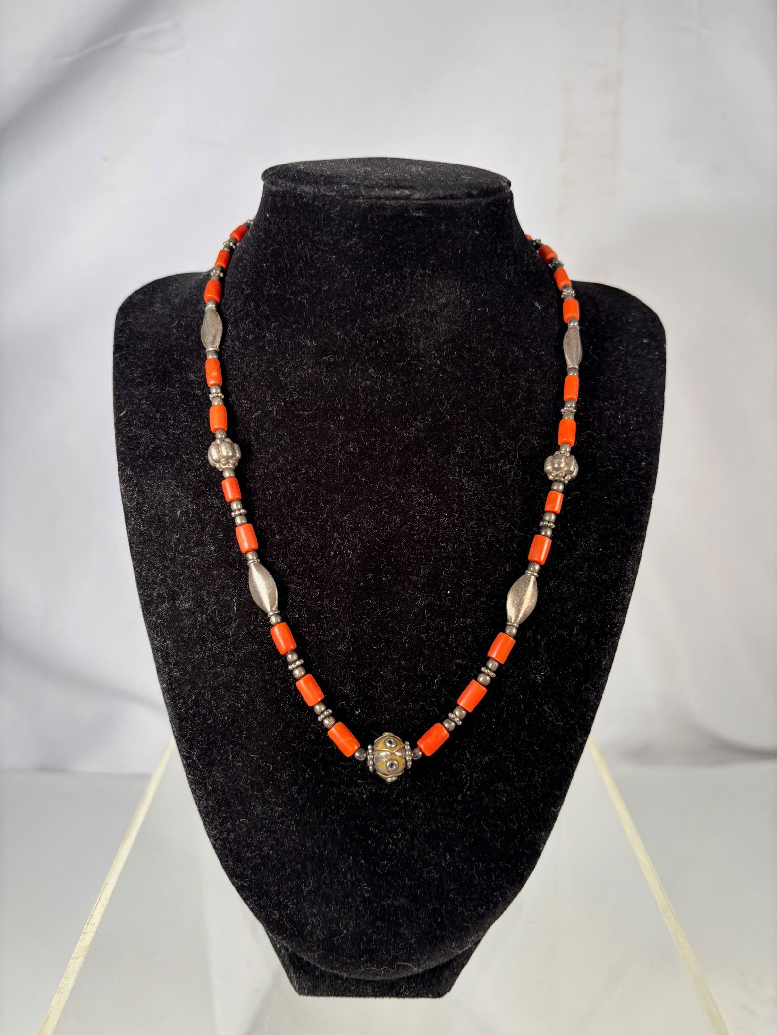 A Coral Bead Necklace with Silver Beads: Necklace composed of small cylindrical coral beads interspersed with silver beads and decorative spacer elements. Finished with an S-hook clasp. Necklace Length: 18 inches.
