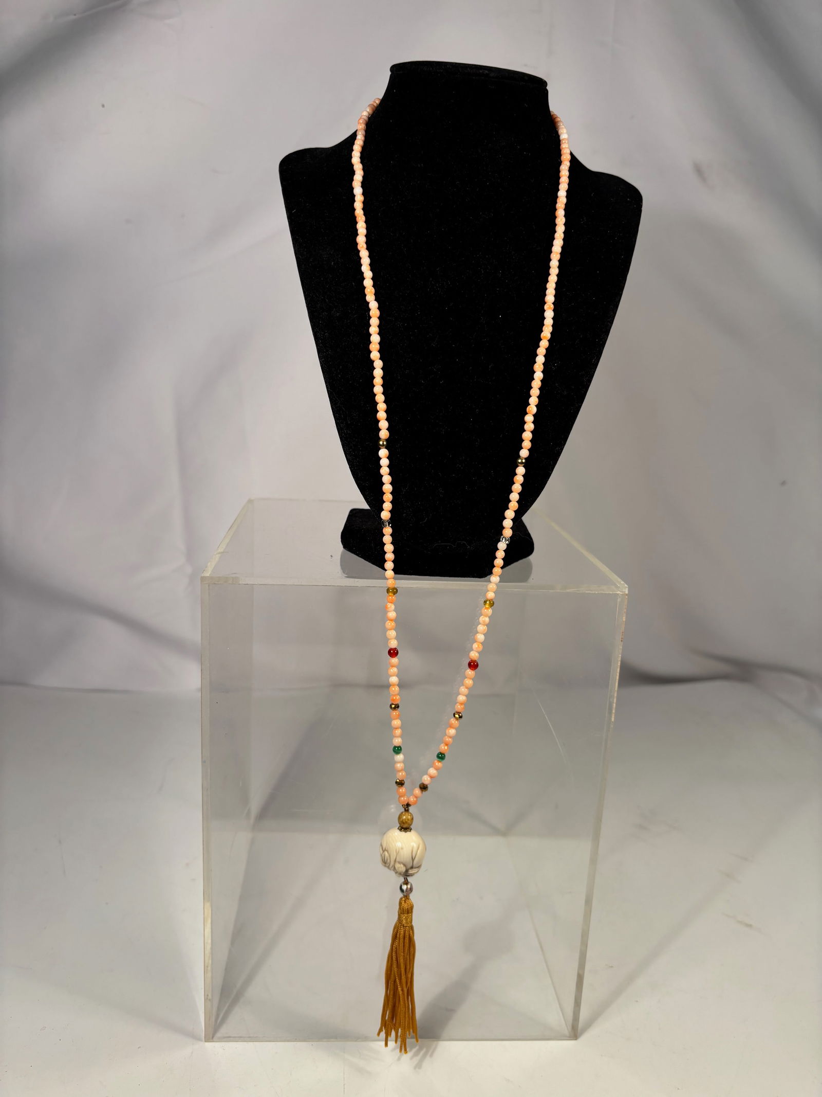 A Long Pink Coral Bead Necklace with Carved Bone Pendant and Tassel, 31 in.: Long strand necklace composed of small pink coral beads with assorted glass and metal accent beads. The necklace suspends a carved bone pendant and decorative tassel. Overall length approximately 31 i