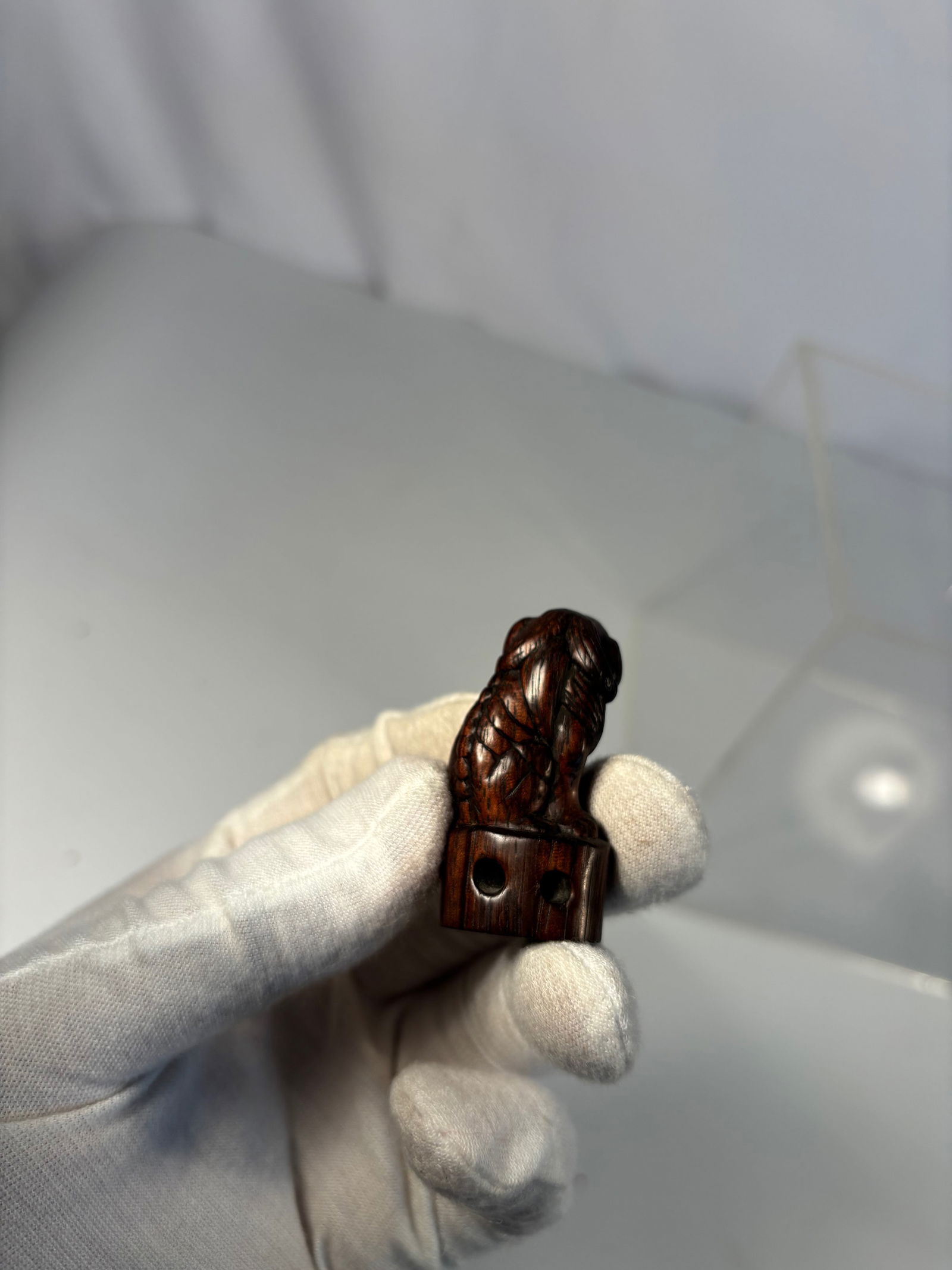 A Japanese Carved Wooden Lion Netsuke, signed Gan Yu: Meiji period (1868–1912); Finely carved from wood as a seated lion (komainu), with detailed features and natural patina. The base with himotoshi cord holes, also incised with the characters “Gan Y