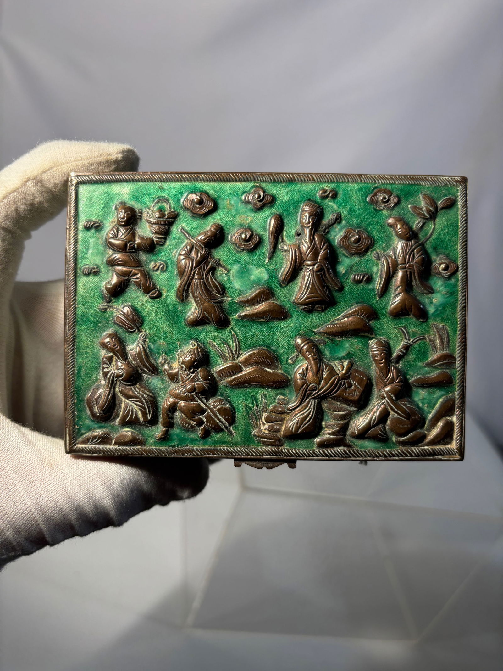 A Chinese Gilt Metal & Green Enamel Figural Relief Decorative Box: Chinese gilt metal decorative box with vibrant green enamel ground, featuring high relief figural scenes on the lid and sides. The surface is richly adorned with molded and gilt figures in traditional