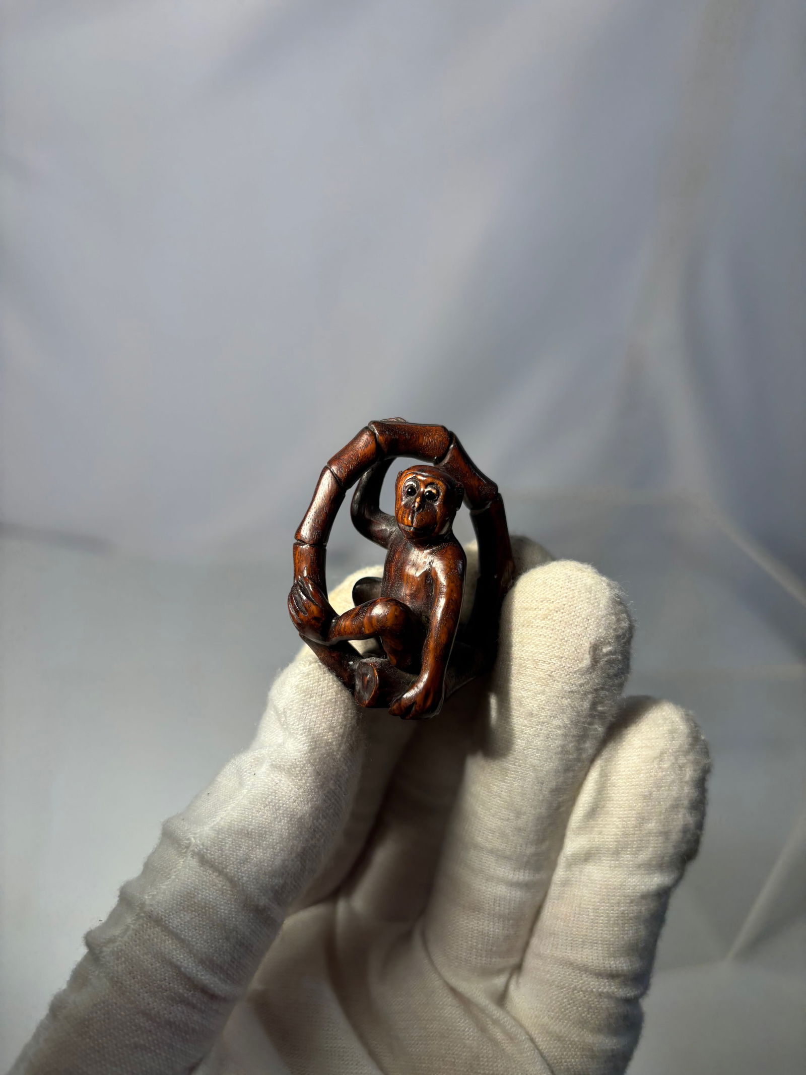 A Carved Monkey Figure with Bamboo Form with mark: Carved figure of a seated monkey holding a stylized bamboo-form ring. Finely polished surface with rich reddish-brown tone. The eyes inset with dark beads. Incised signature to side. Height: 2 inches.