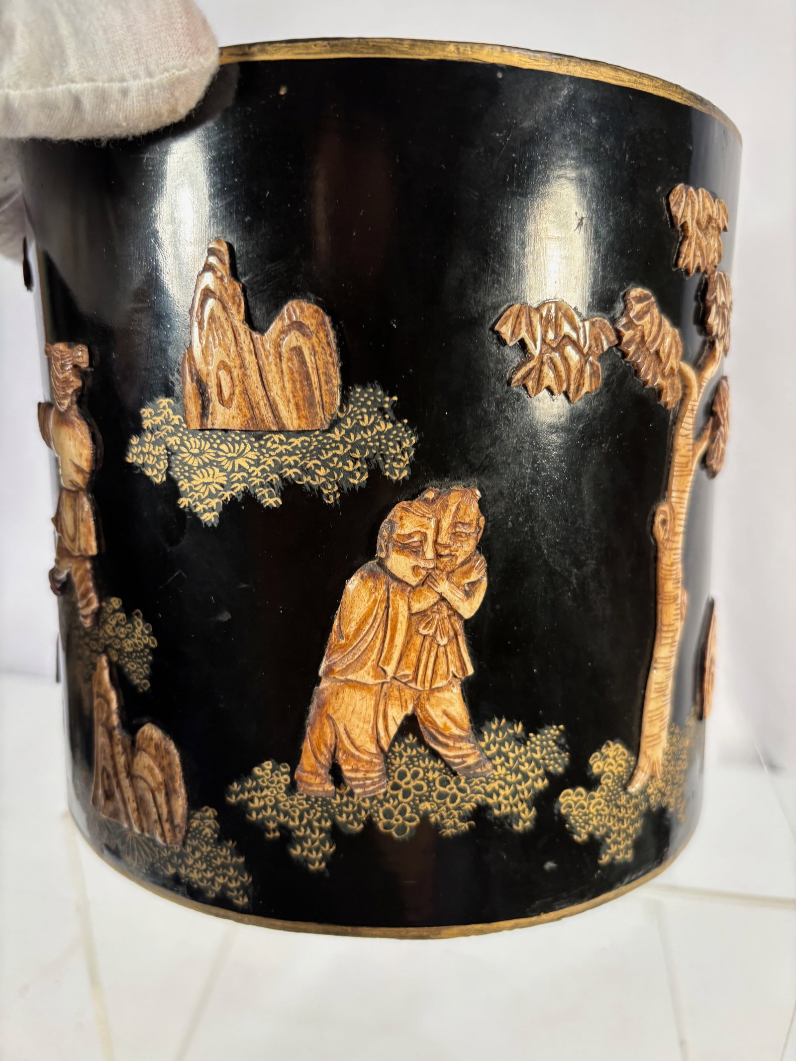 A Chinese Black Lacquer Brush Pot with Gilt Figural Decoration: 20th century, Chinese black lacquer brush pot decorated in relief with gilt figures in a landscape. Likely resin or composite material with lacquer coating.The underside bears a “Made in China&rdquo