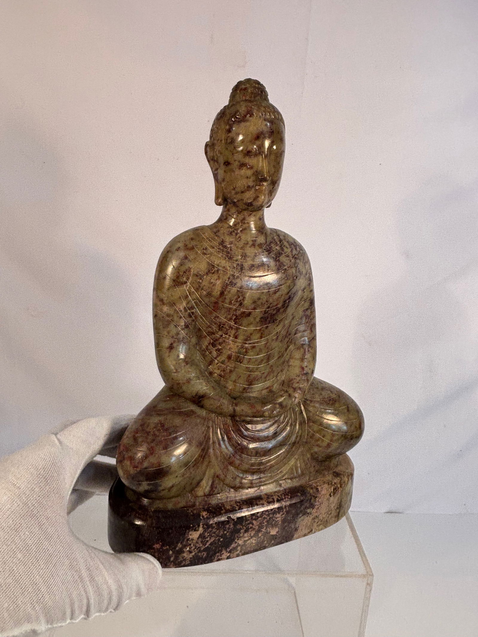 An Asian Carved Stone Seated Buddha: Late 19th to Early 20th century. A carved stone figure of the Buddha, The figure is depicted seated in meditation (dhyana mudra) on an integral oval base, with elongated features, downcast eyes, and l