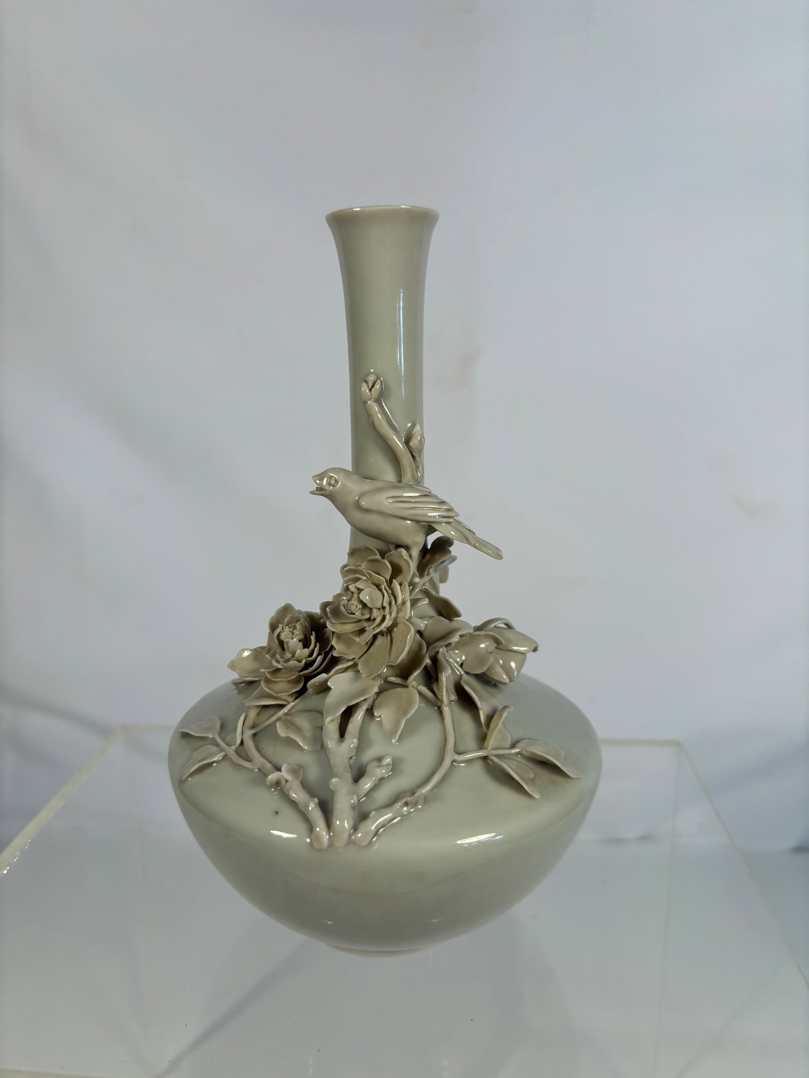 A Chinese Celadon-Glazed Vase with Applied Bird and Flower Decoration: Qing Dynasty(1644-1912); The vase with a globular body rising to a tall slender neck and flared rim, applied in high relief with a bird perched on flowering branches issuing peony blossoms and leaves,