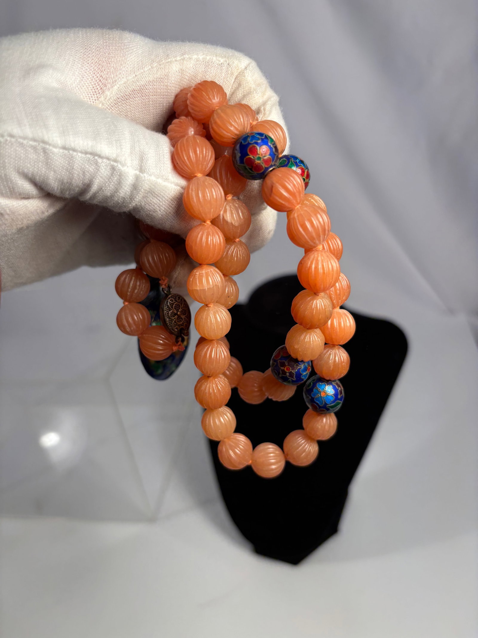 A Chinese Carved Agate Bead Necklace with Silver Cloisonné Enamel Vase Pendant: A necklace strung with ribbed melon-form carved orange agate beads, accented with spherical cloisonné enamel beads of rich blue, red, and green tones. Suspended at the center is a finely crafted cloi
