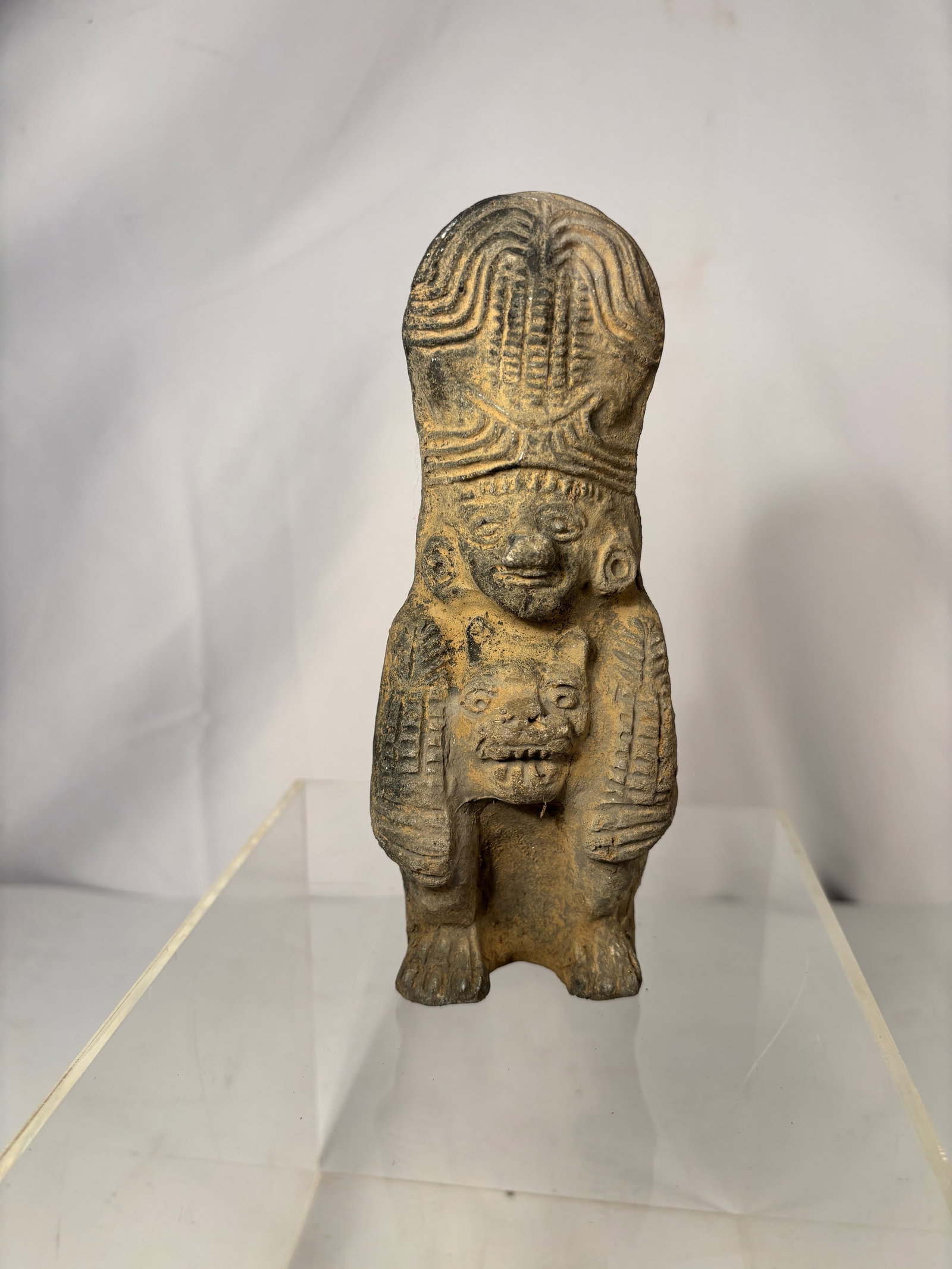 Pre-Columbian Style Hollow-Back Terracotta Figure: Terracotta figure in the style of ancient Pre-Columbian Mesoamerican art, depicting a standing figure with a tall, stylized headdress and carved decorative details. The figure holds an animal-like cre