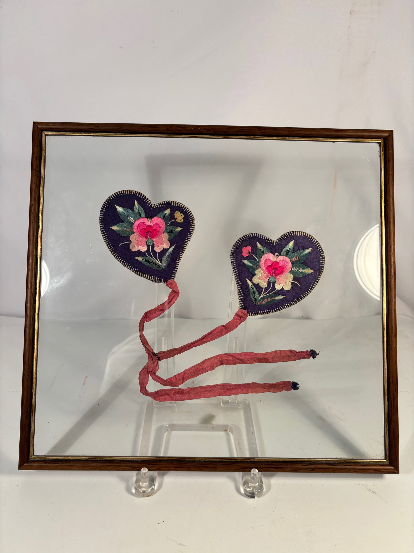 Pair Antique Chinese Heart Shaped Embroidered Silk Fragrance Sachets, framed: Pair of antique Chinese heart-shaped embroidered silk sachets featuring floral decoration on deep blue ground with silk ribbon ties. Likely late Qing period. Presented in a later frame. Frame Dimensio