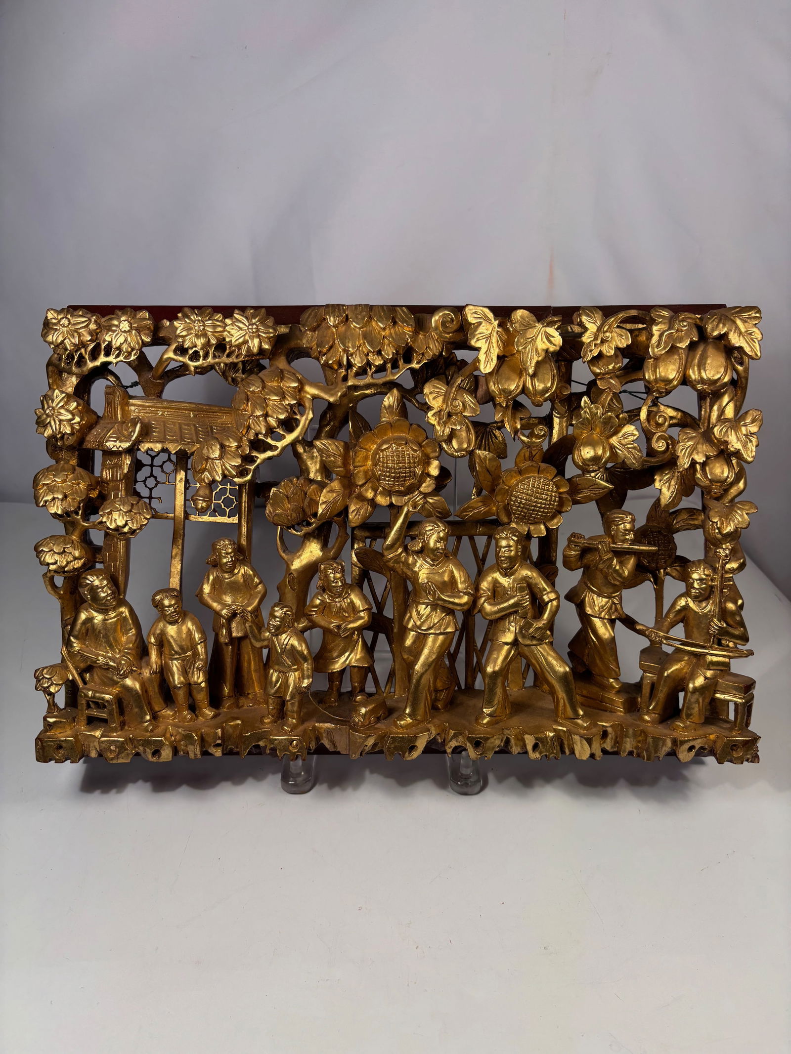 A Chinese Carved Wood Carved Figural Scene Panel: Chinese carved wood panel depicting a courtyard figural scene with gilt decorated figures set within a red lacquer openwork frame. Height: 11 inches; Length: 16 inches.