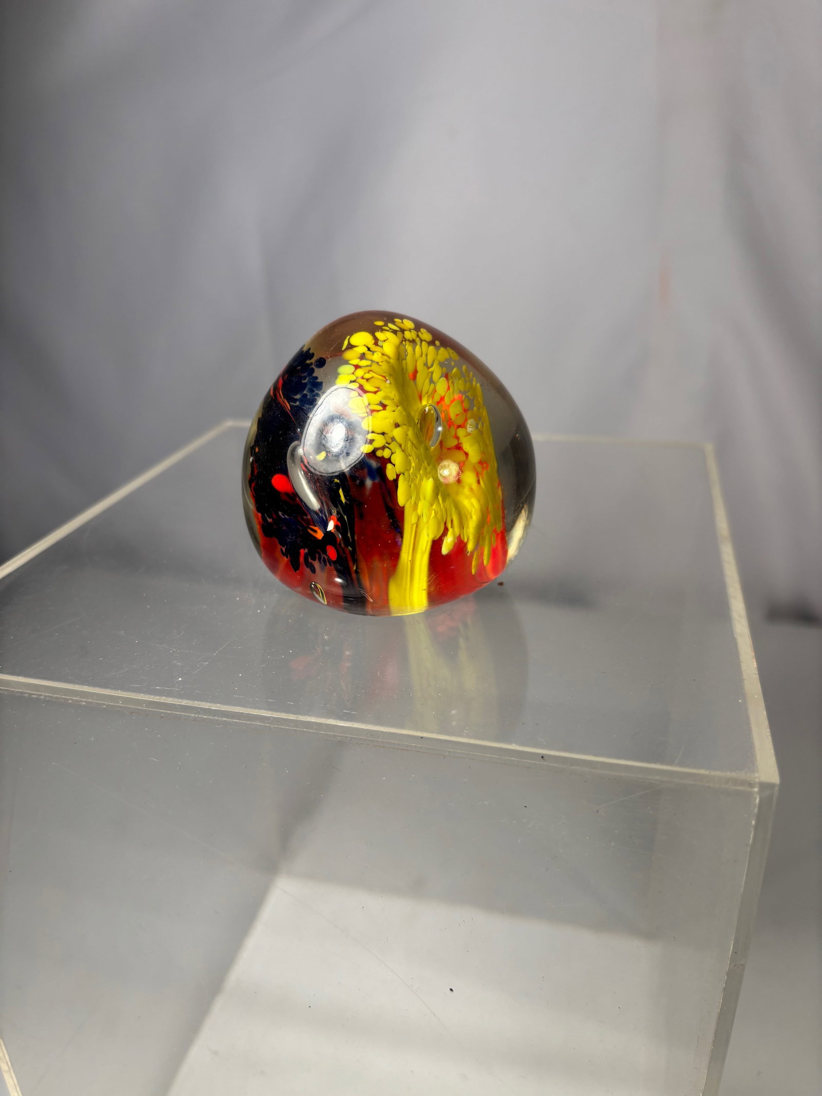 Art Glass Paperweight w/ Yellow & Red Flame / Floral Burst Design: A decorative studio art glass paperweight featuring a vivid internal abstract floral or flame-like design in yellow, red, and black tones, encased within a clear glass dome. The piece displays organic