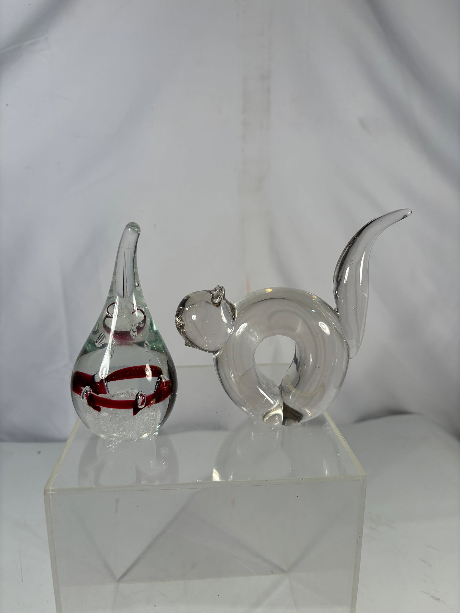 Pair of Studio Art Glass Sculptures w/ Teardrop & Animal Form: A pair of modern studio art glass decorative pieces, including a teardrop-form sculpture with internal red band and bubble inclusions, and a clear glass animal figure with curled body and applied deta