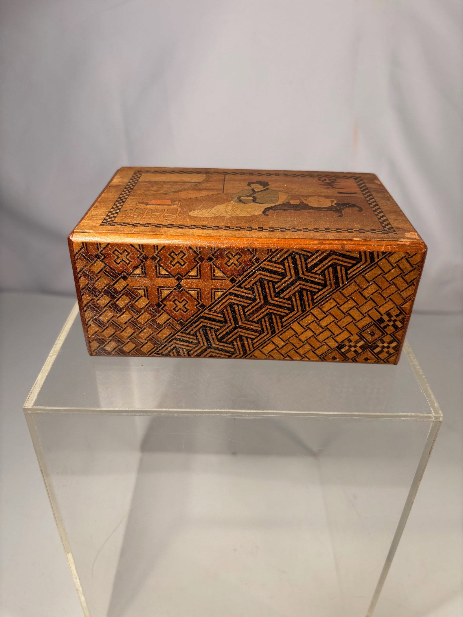 A Japanese Hakone Yosegi Puzzle Box (Himitsu-bako): Japanese wooden puzzle box decorated with traditional yosegi zaiku marquetry composed of various natural woods forming geometric mosaic patterns. The box opens through a sliding panel mechanism typica