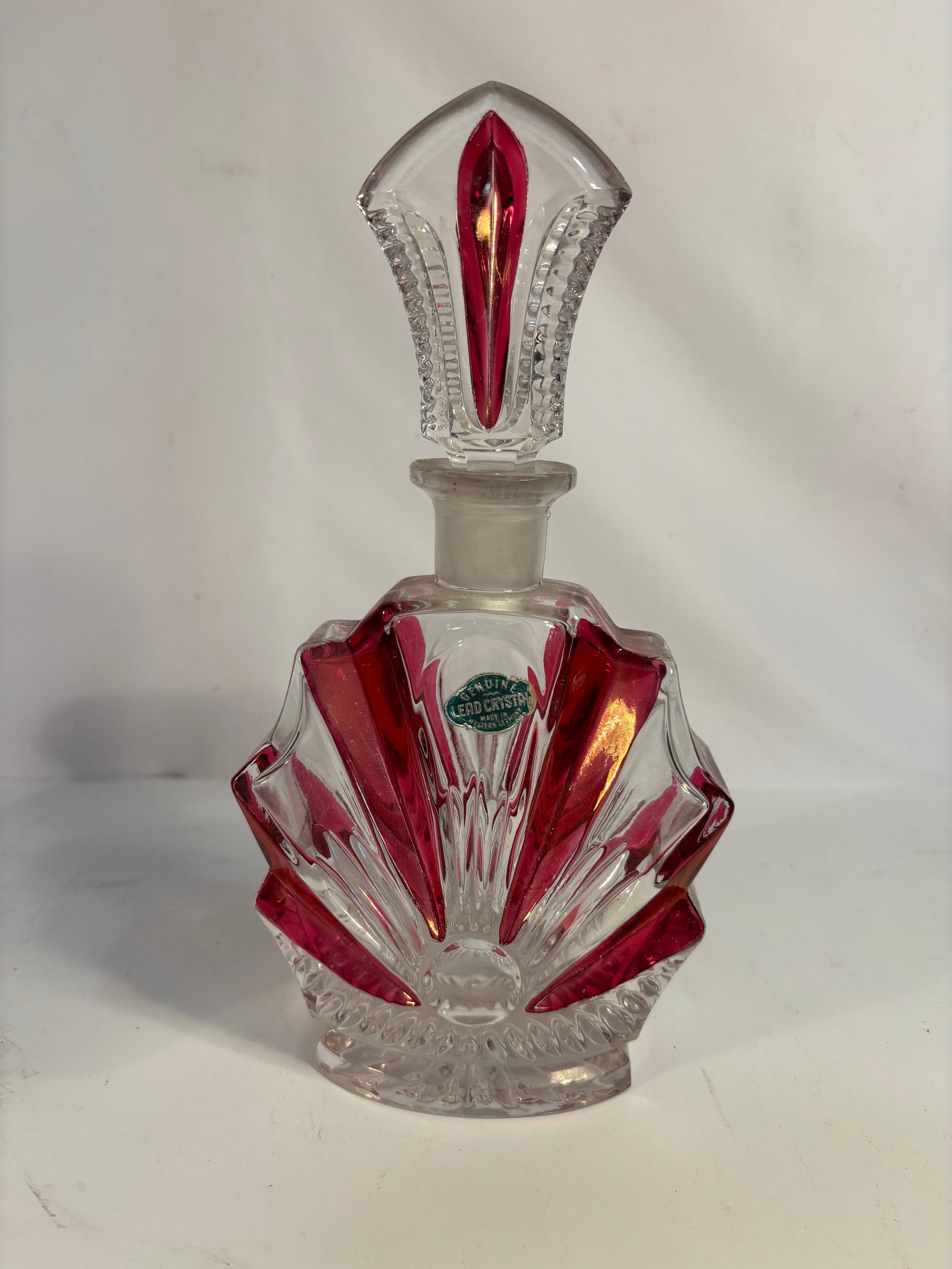 A Large West German Ruby Cut-to-Clear Lead Crystal Perfume Bottle, c. 1950–1970: Elegant West German lead crystal perfume bottle, circa 1950s–1970s, showcasing a vivid ruby red cut-to-clear design in a stylized fan or shell shape. The bottle features deep geometric cuts radiatin
