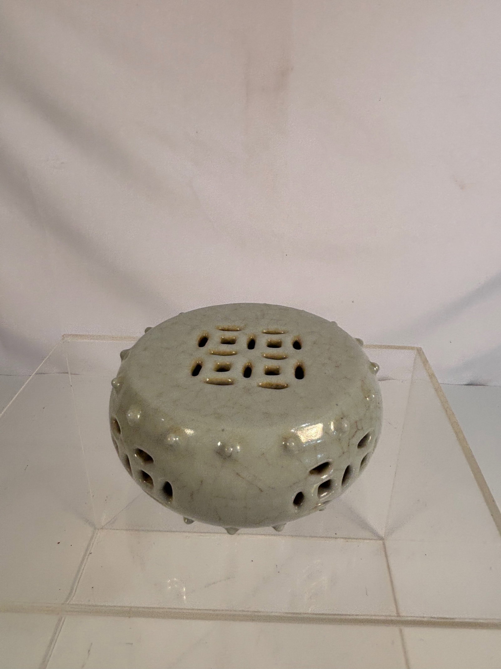 A Chinese Celadon-Glazed Pierced Incense Burner, Ge-Type Crackle, with Qianlong Mark: A celadon-glazed ceramic incense burner of rounded drum form with small applied bosses around the sides. The cover and sides pierced with geometric apertures for ventilation, covered overall in a pale