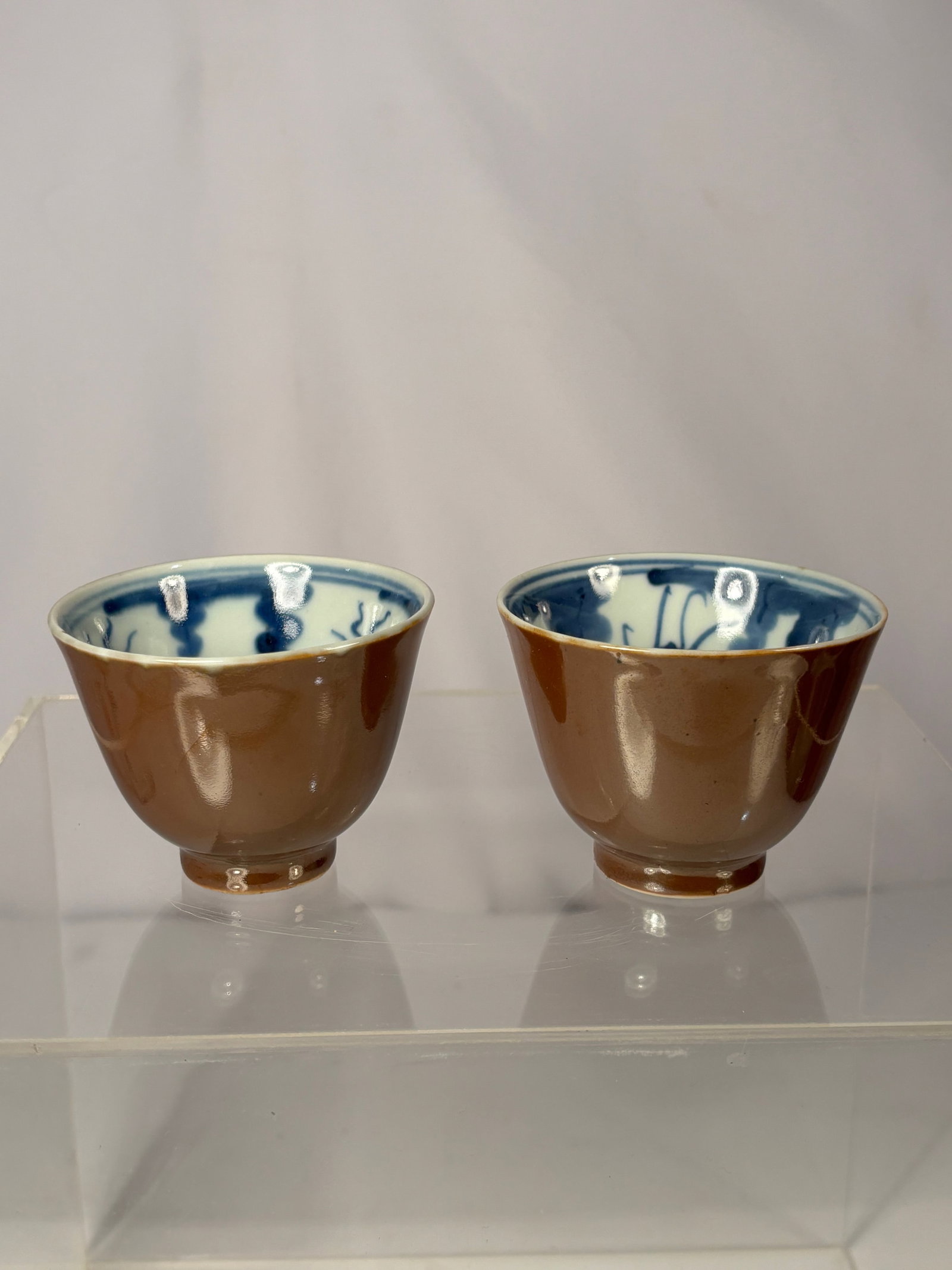 Pair of Chinese Brown-Glazed Cups with Blue and White Interior: Qing dynasty(1644-1912) ;A pair of Chinese porcelain teacups featuring a glossy brown exterior glaze and hand-painted blue and white decoration on the interior. Each cup has a neatly finished foot rim