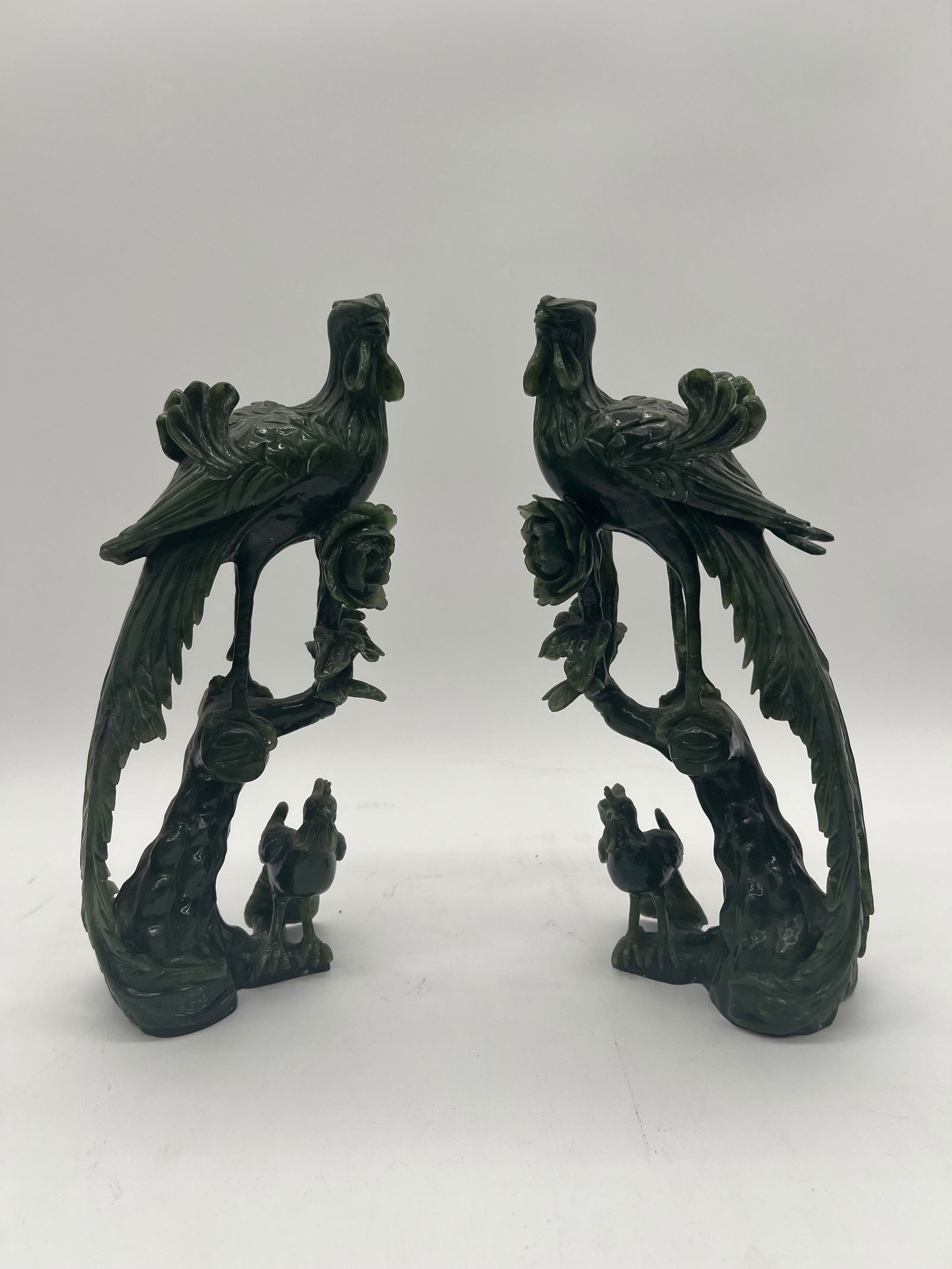 A pair of Chinese green jade bird sculptures: Late 19th century to early 20th century; The carvings depict birds, likely phoenixes or peacocks, perched on trees with human figures at the base. Dimensions?Height: 10.5 inches