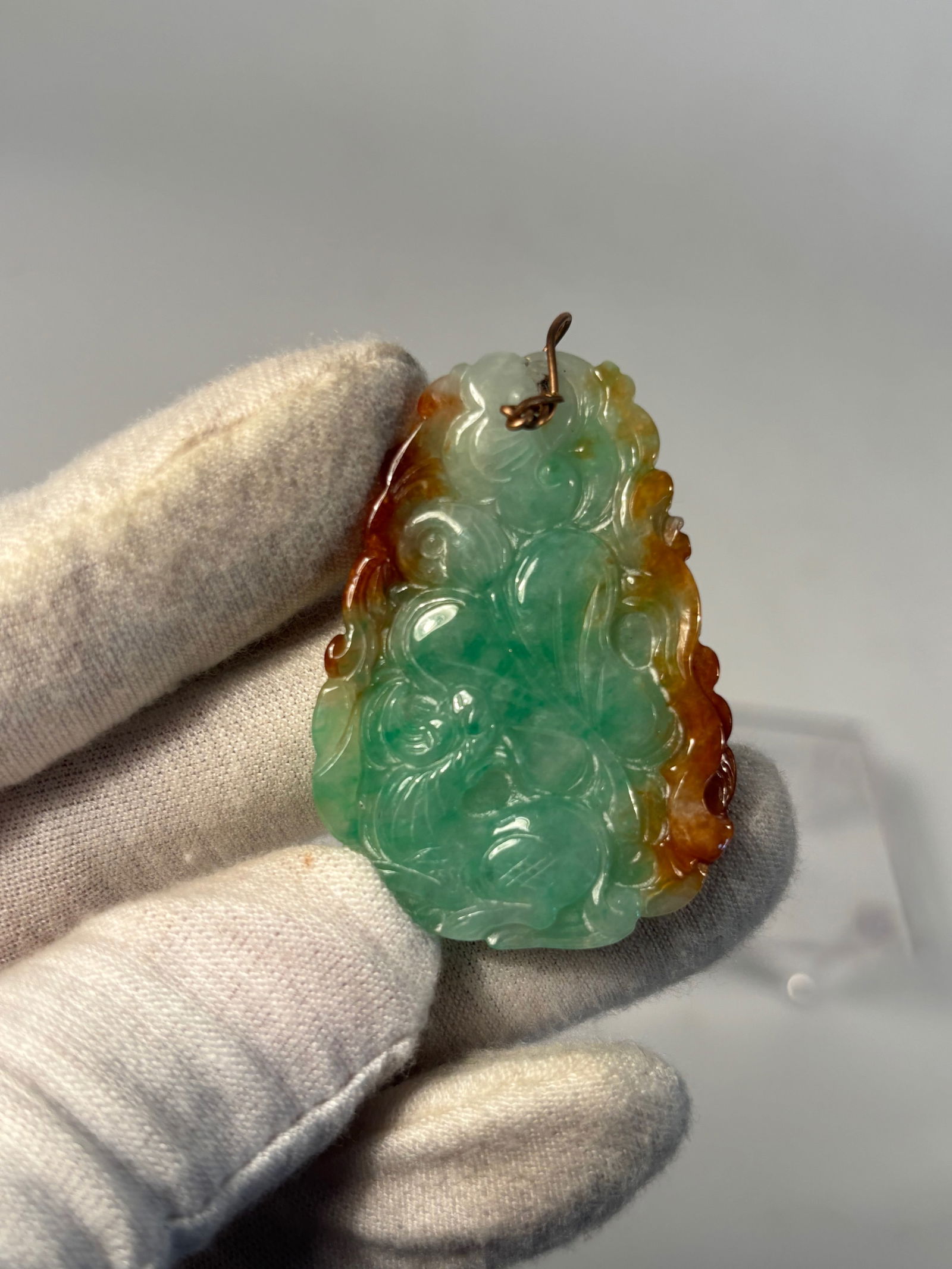 A Chinese Carved Jadeite Pendant with Russet and Green Colors: Qing Dynasty (1644-1912); A Chinese jadeite pendant, skillfully carved with auspicious cloud scrolls and bat motifs, symbolizing happiness and good fortune. The stone features vibrant apple-green tone