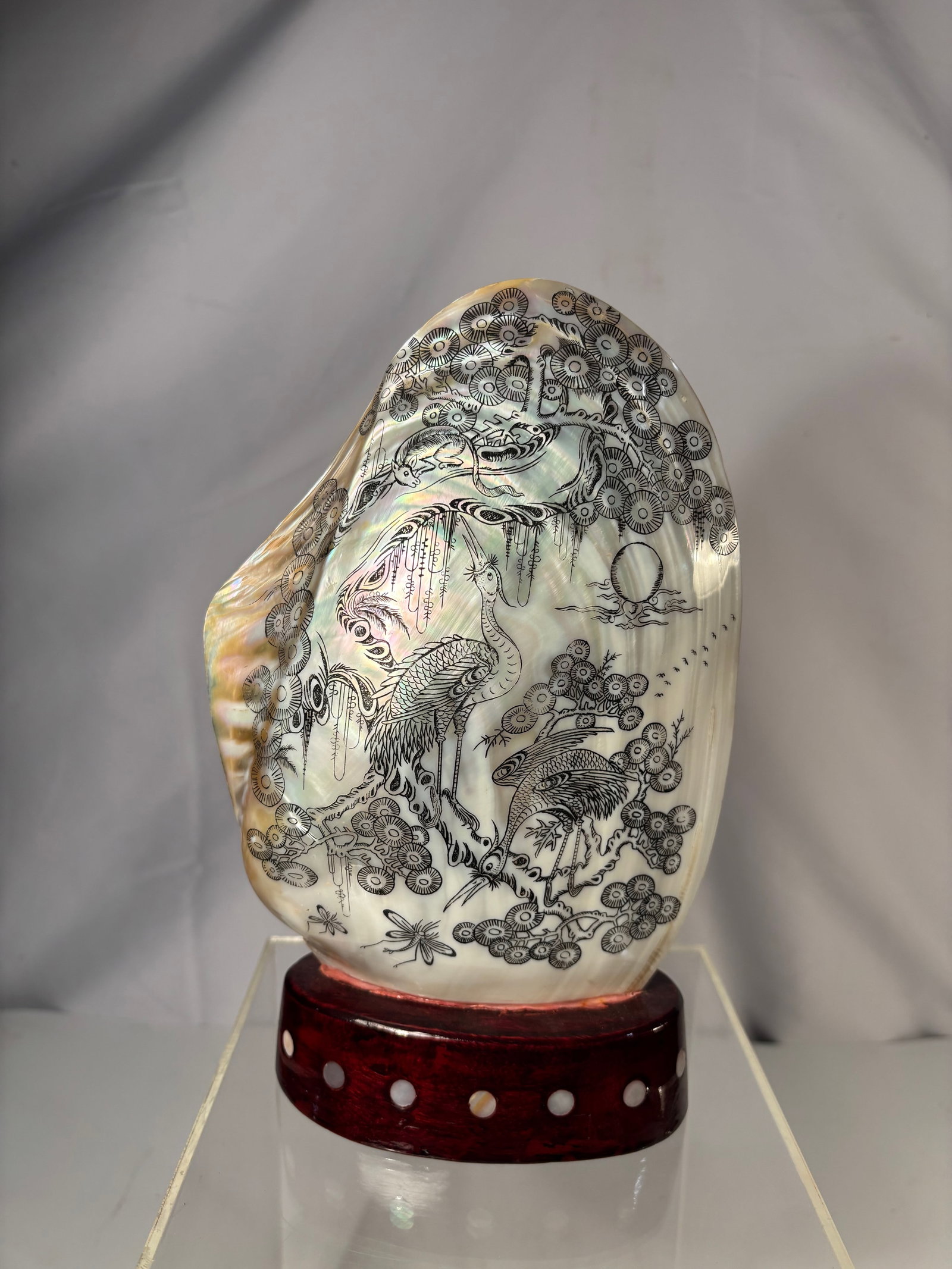 A Chinese Engraved and Painted Mother-of-Pearl Shell with Crane and Pine Design on Stand: Decorated mother-of-pearl shell featuring finely engraved and painted imagery of cranes among pine trees. The iridescent surface of the shell enhances the detailed linework and gives depth to the land