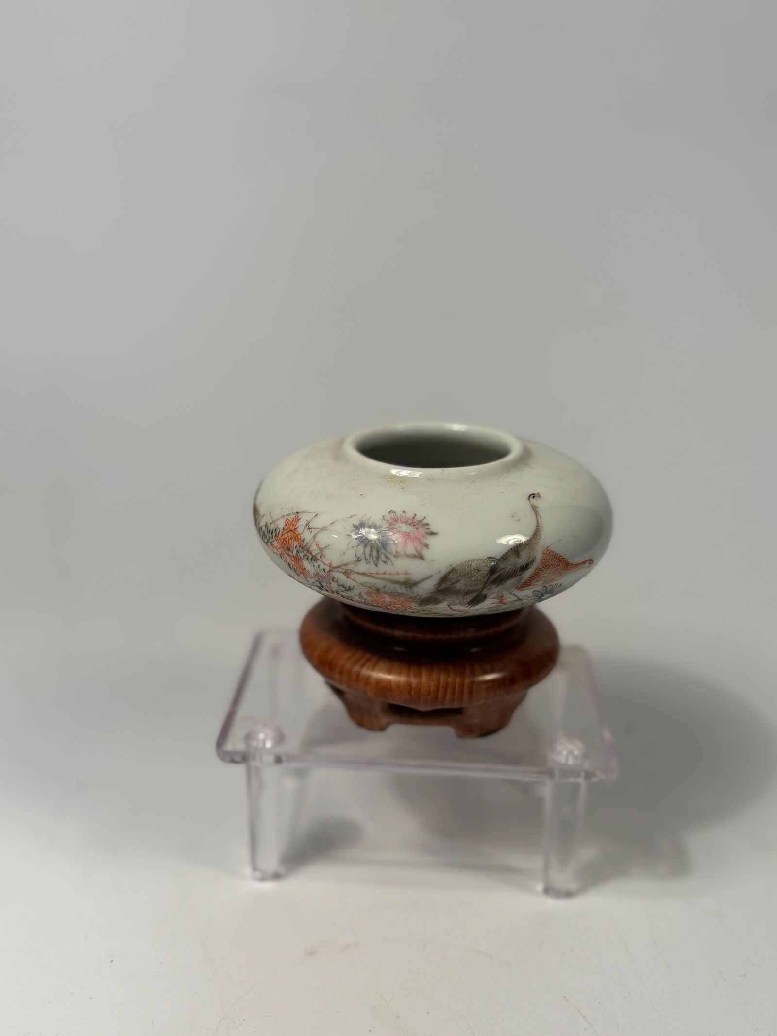 A Chinese Famille Rose Porcelain Brush Washer with porcelain Stand imitating appreance of wood: 18th century; A Chinese porcelain brush washer or waterpot, of compressed globular form, finely enameled in the famille rose palette. The body features a continuous scene of cranes walking among bloom