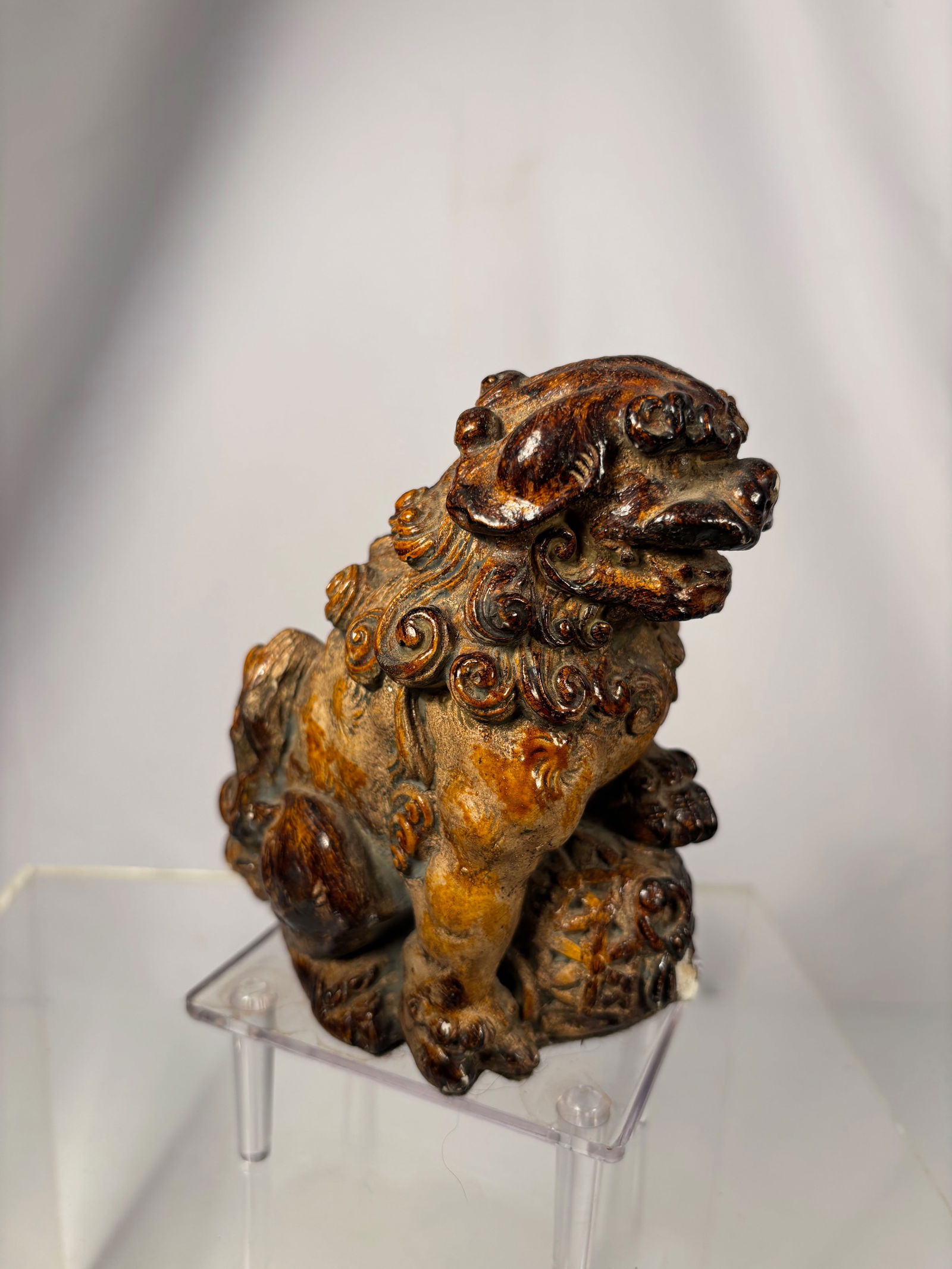 A Chinese Sancai-Glazed Ceramic Guardian Lion, Ming Dynasty or earier: Ming Dynasty(1368-1644); Seated in a powerful pose with the head turned slightly to one side, the guardian lion modeled with bulging eyes, open mouth, and detailed curling mane, one forepaw resting pr