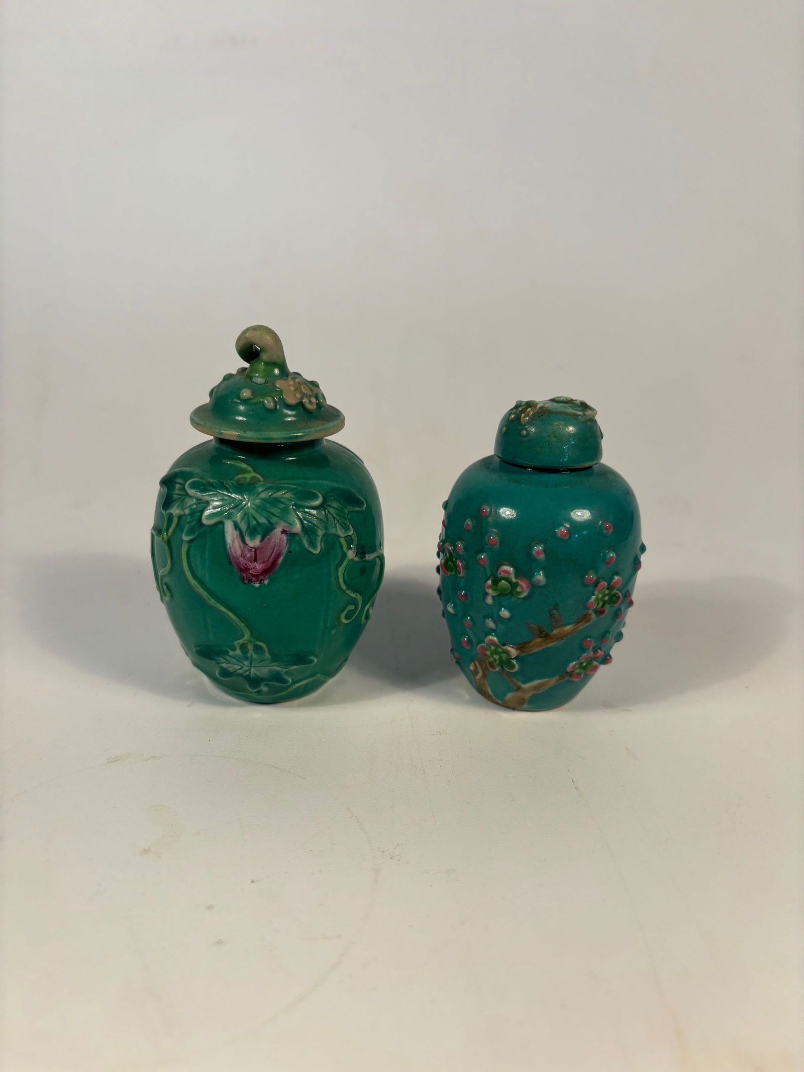 Set of two Chinese Green-Glazed Relief Porcelain Jars: Qing Dynasty (1644-1912);A charming set of antique Chinese porcelain jars, each covered in a rich green glaze with applied relief decoration. One jar features a lotus flower and foliage motif with a d