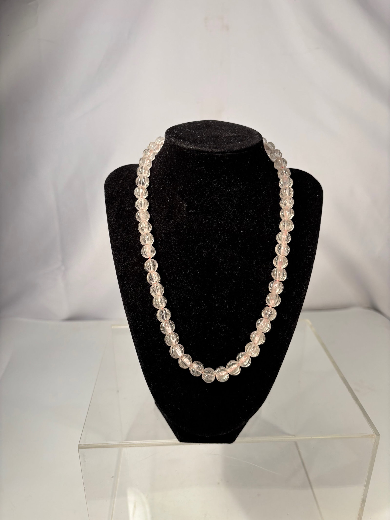 A Clear Rock Crystal Bead Necklace with Gold-Tone Clasp: This necklace is composed of clear carved beads, each formed in a melon-style shape with longitudinal grooves. The beads are transparent to lightly translucent, showing natural internal inclusions and